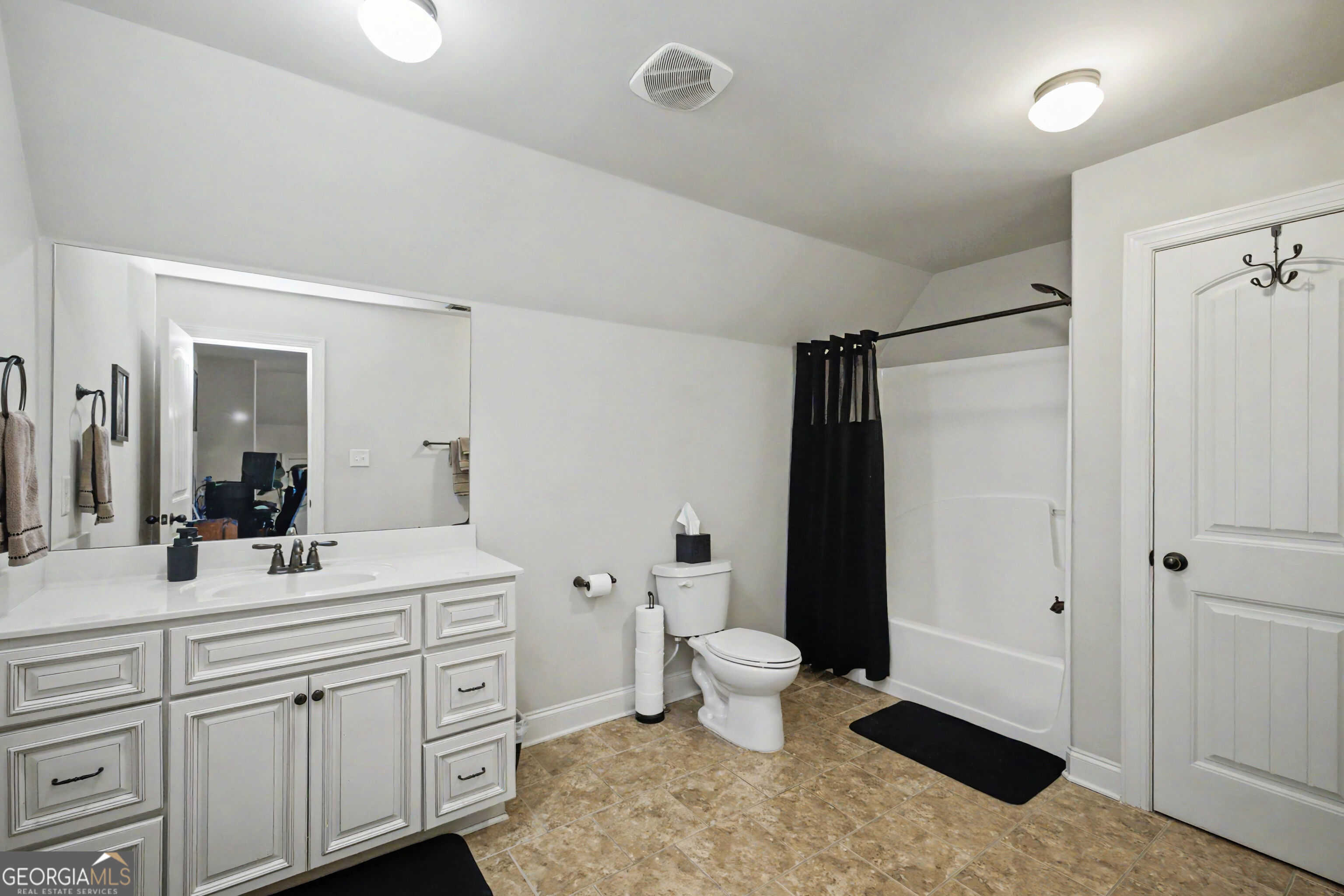 Bathroom with a white paneled vanity, tan tile floor, and bathtub behind a black shower curtain.
