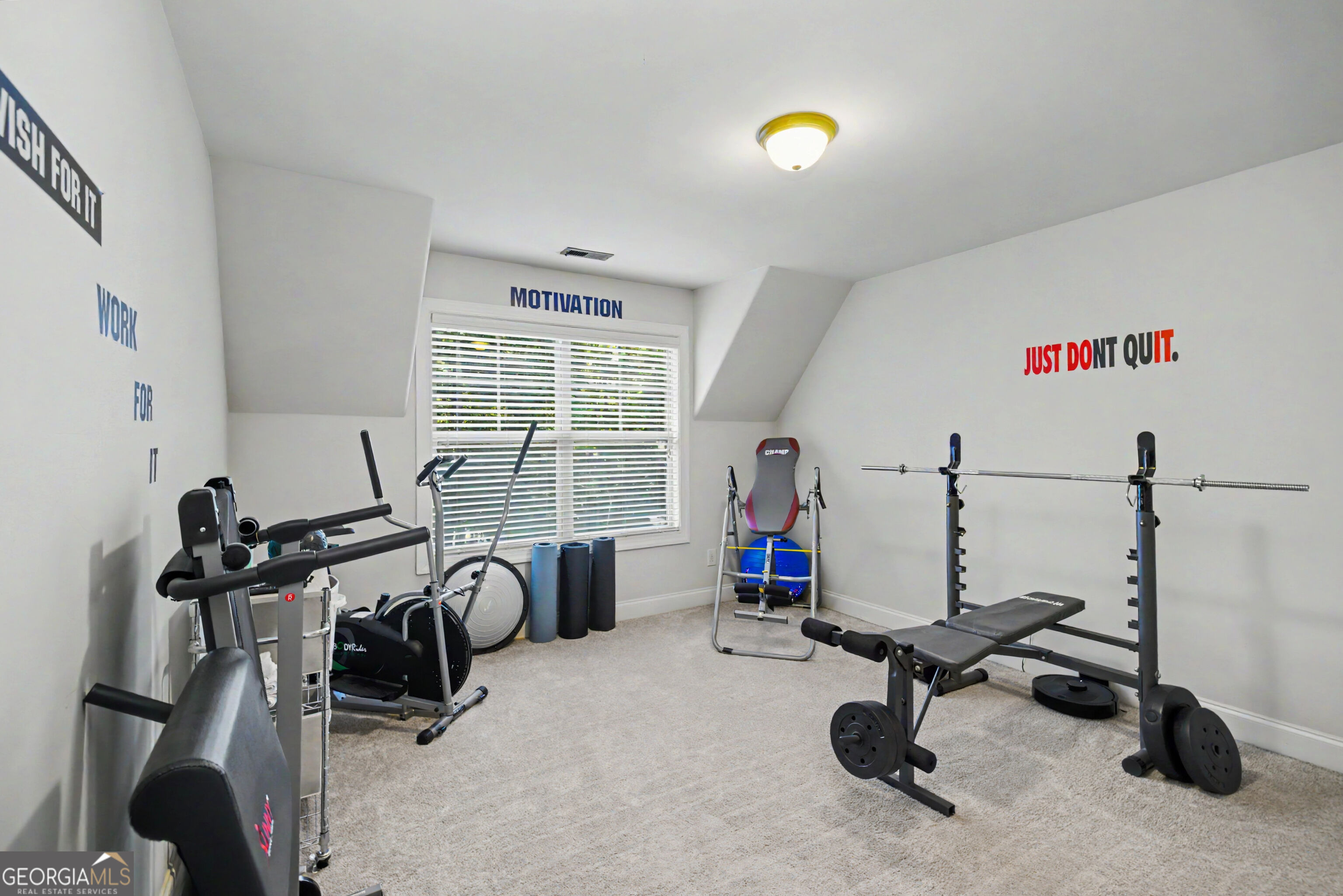 Home gym with a weight bench, barbell rack, exercise machines, and motivational wall lettering.