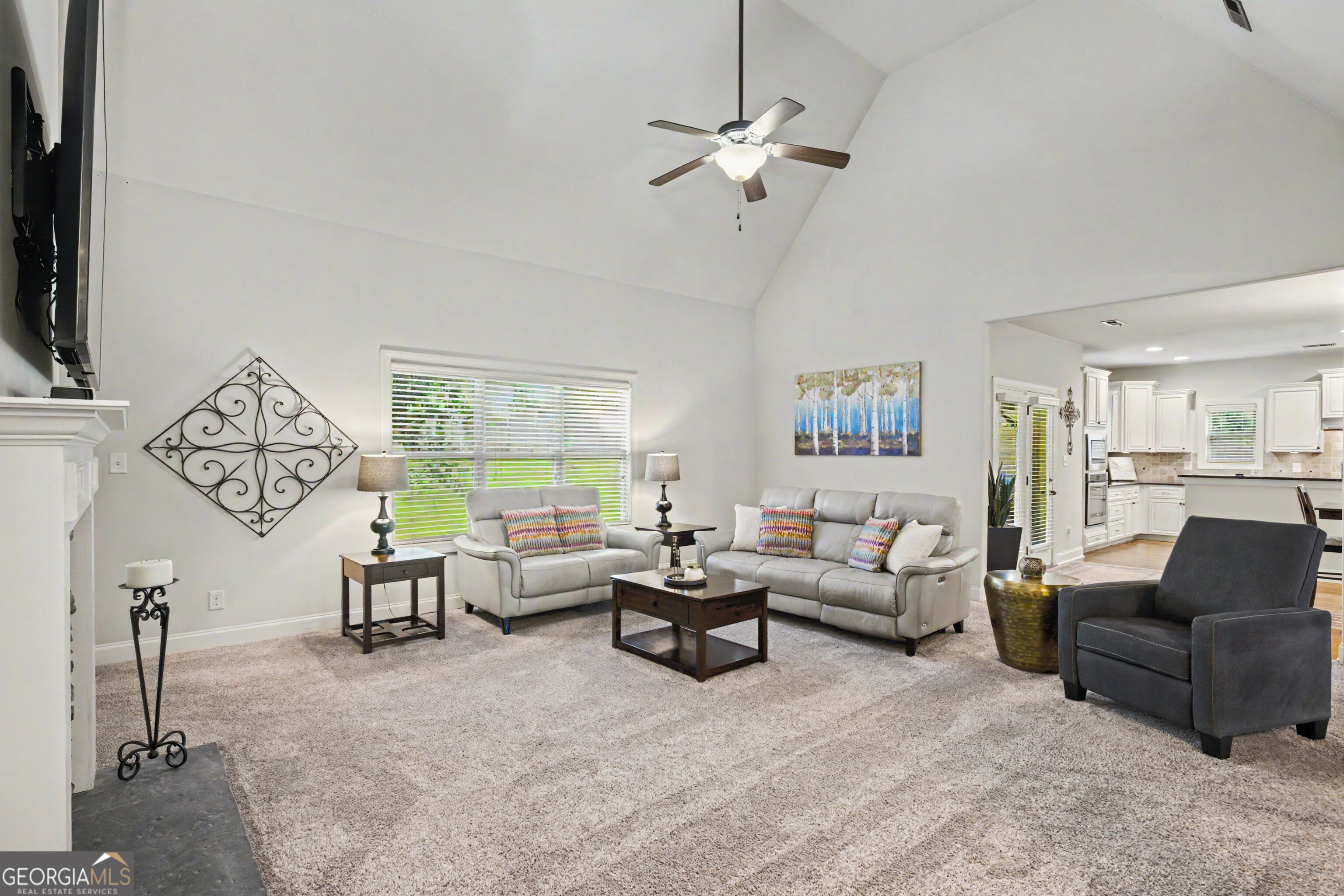 Vaulted living room with light sofas, a dark coffee table, and an open view into the kitchen.
