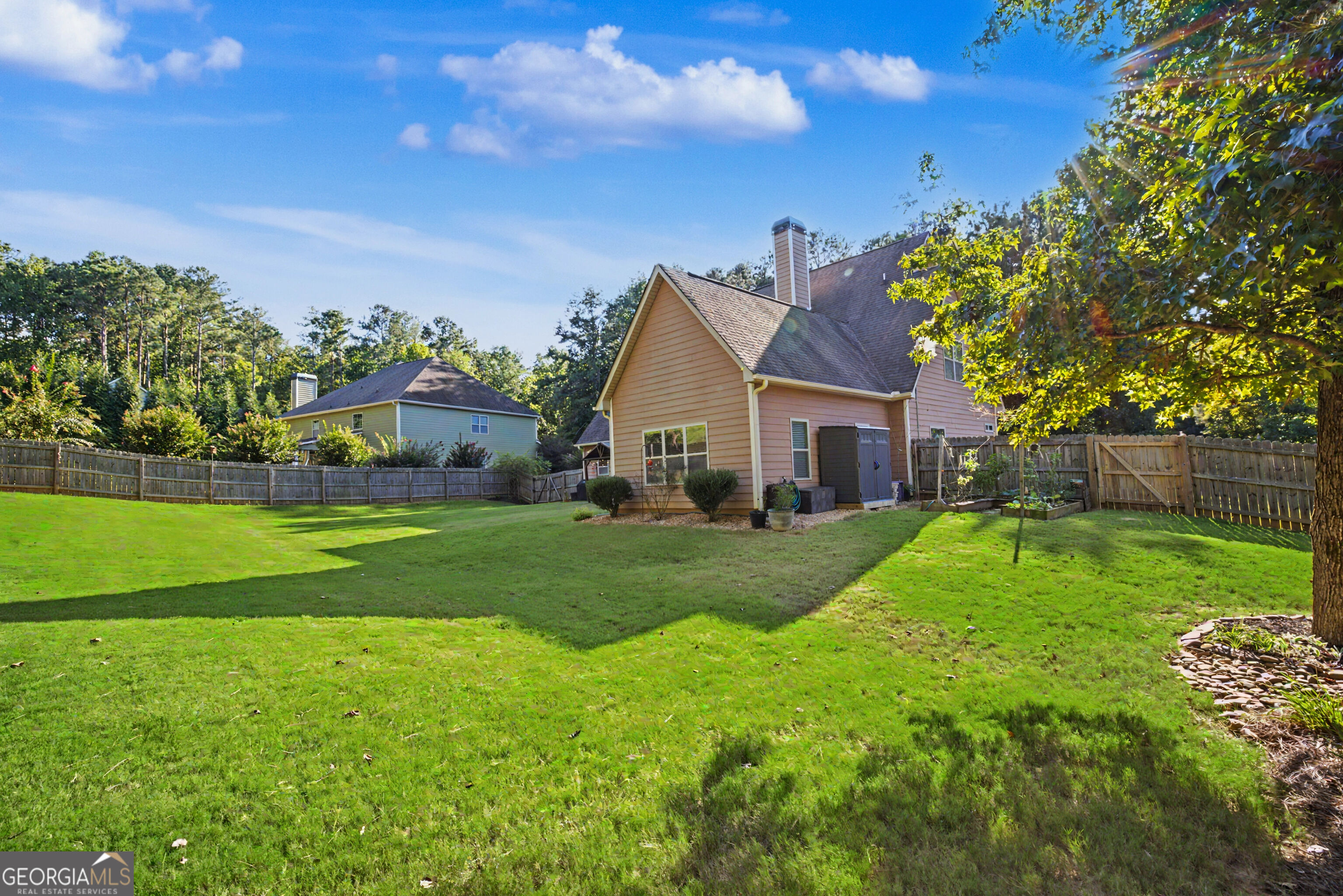 Home’s rear exterior and spacious fenced lawn, with mature trees and garden beds.