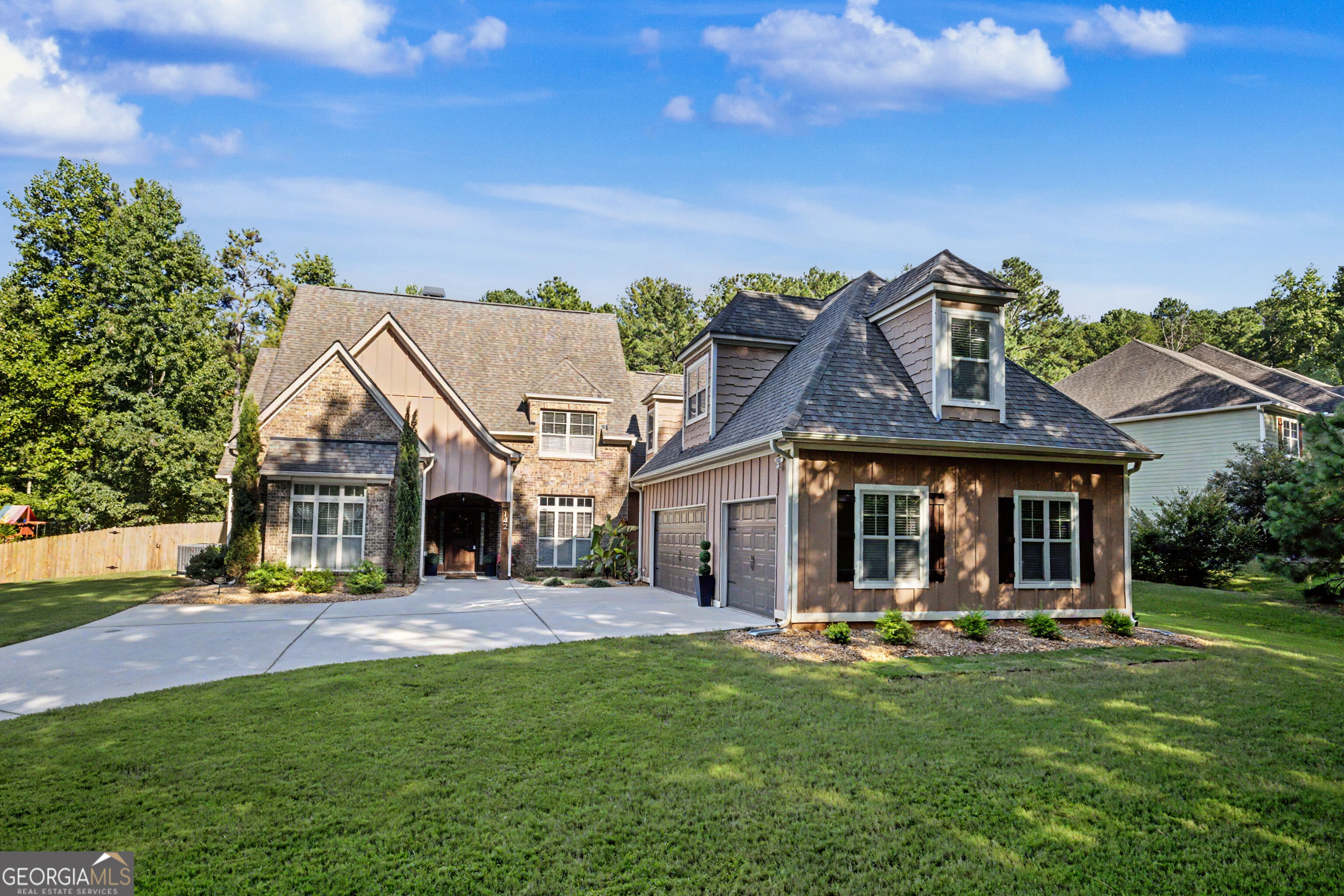 Brick-and-siding home with multiple gables, attached garage, broad driveway, and lawn.