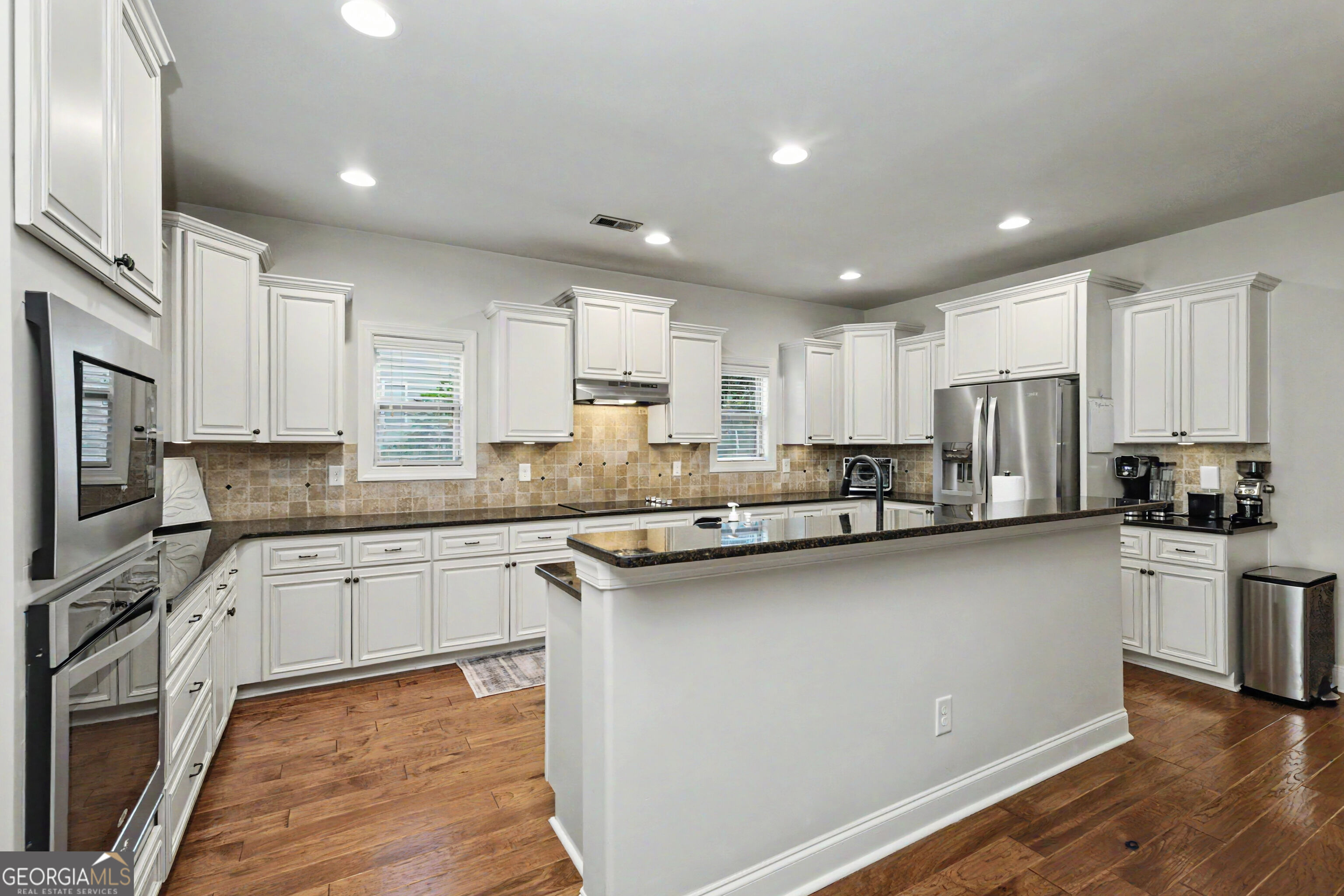 Kitchen with white cabinetry, stainless steel appliances, and a large granite-topped island.