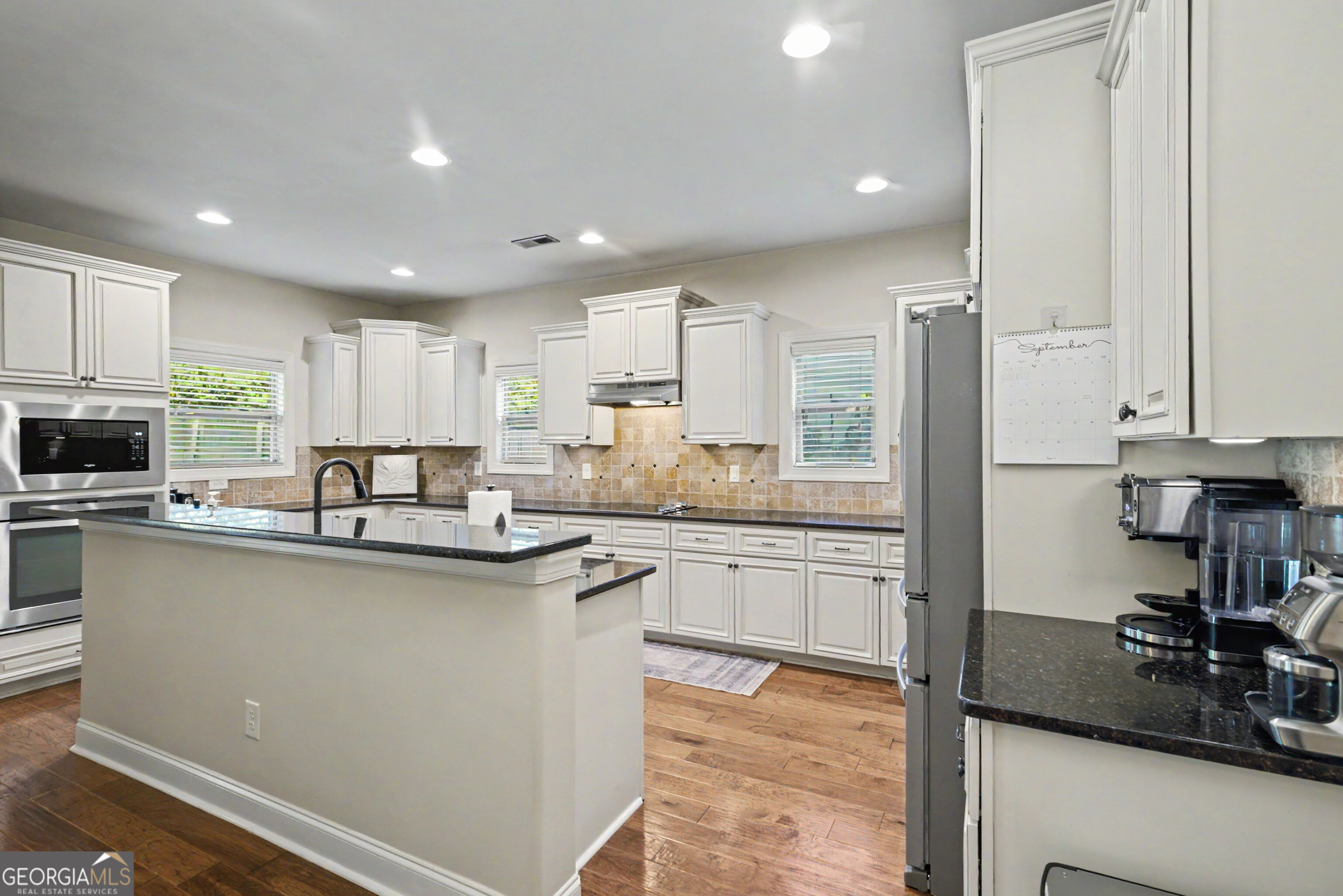 Kitchen with white cabinetry, granite island, tan tile backsplash, and stainless-steel appliances.