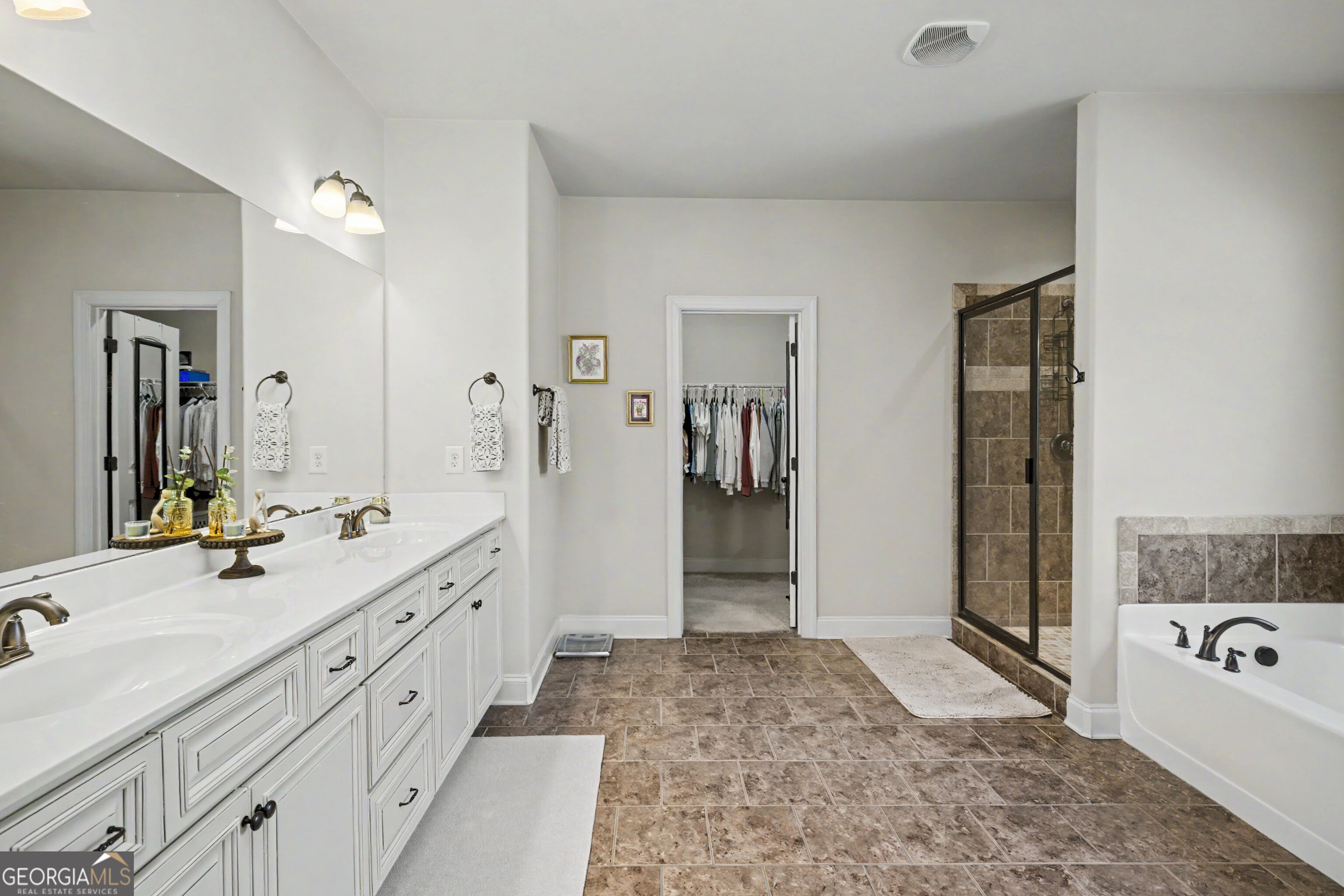 Primary bathroom with a long white vanity, tiled shower, soaking tub, and doorway to a walk-in closet.