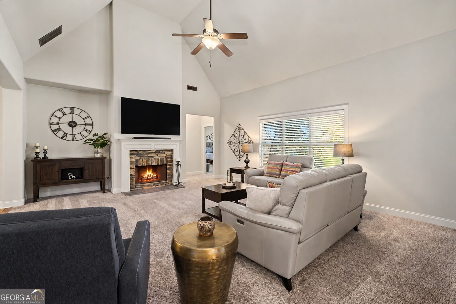Furnished living room with a vaulted ceiling, stone fireplace, and large window.