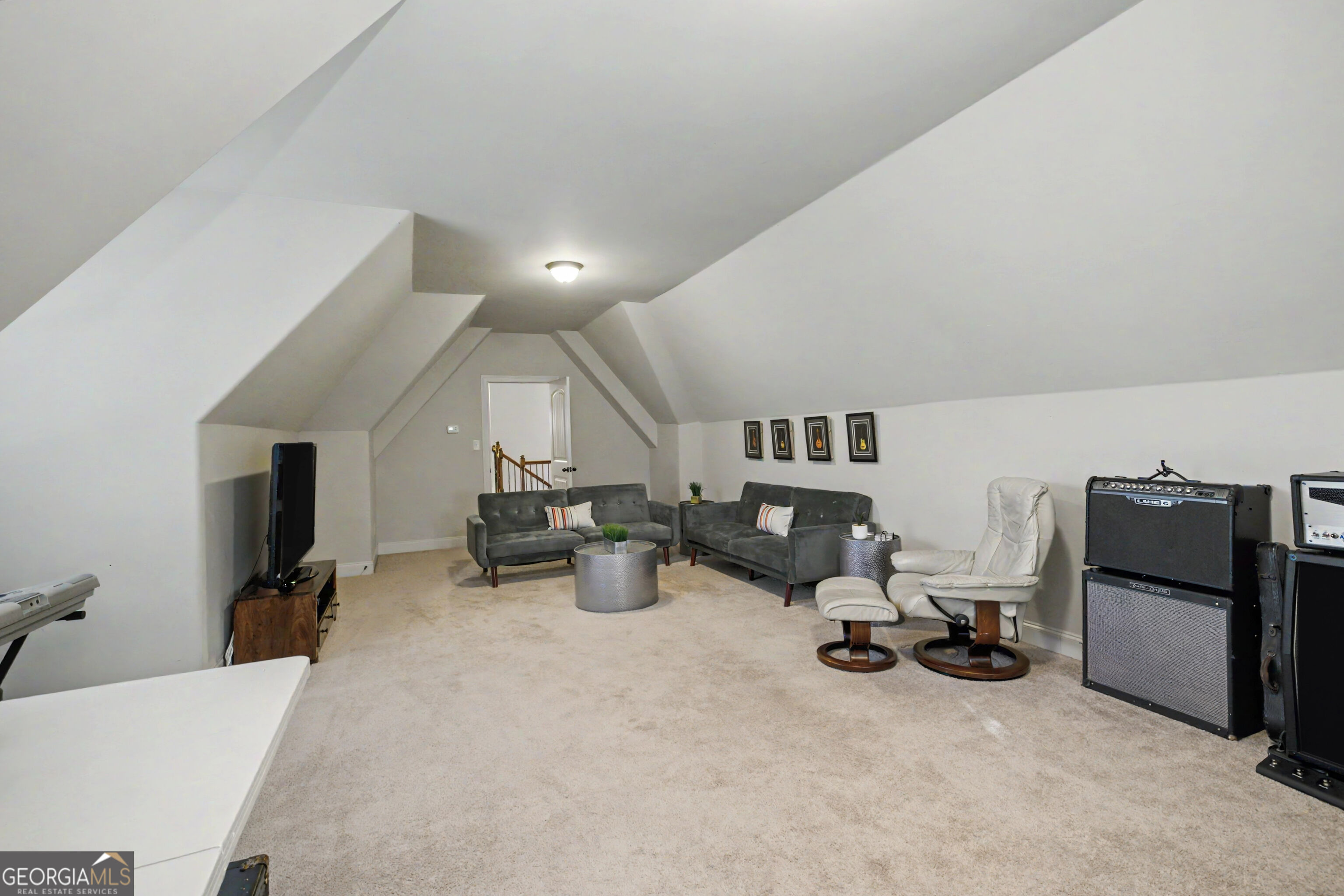 Furnished bonus room with sloped ceilings, gray sofas, a white recliner, and guitar amplifiers.