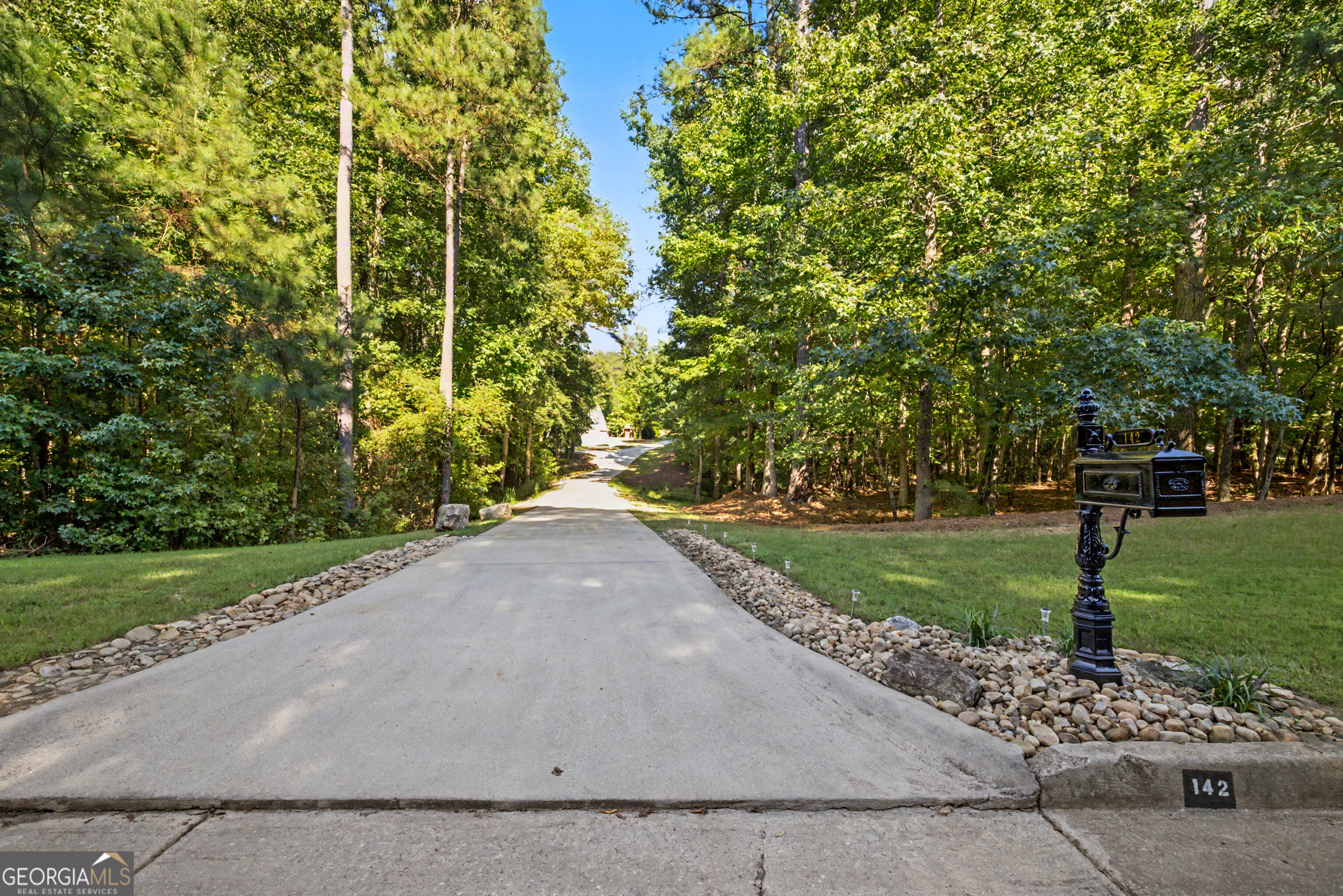 Wooded home driveway with stone borders and a decorative mailbox marked 142.