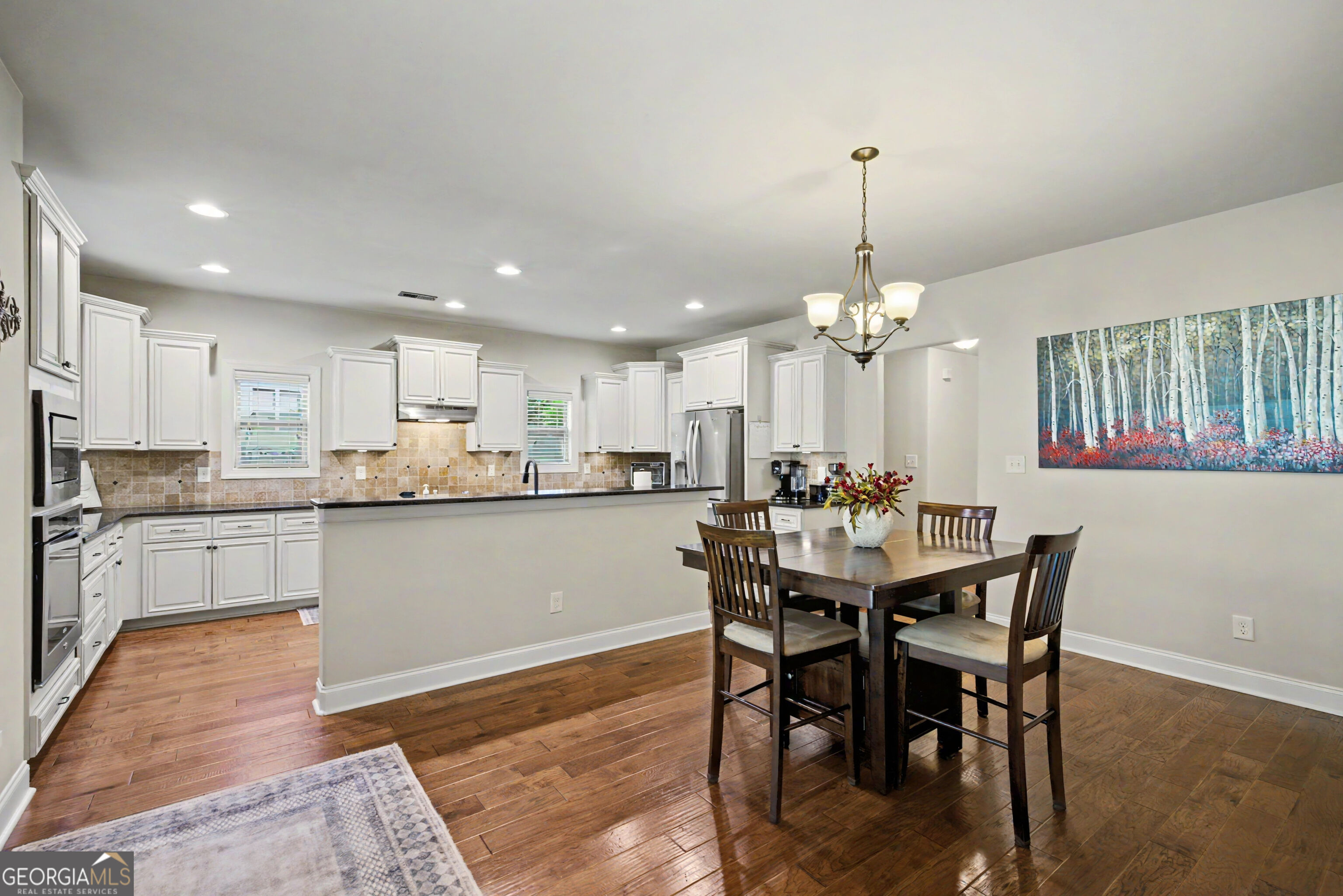 Kitchen and dining area with white cabinets, stainless steel appliances, hardwood floors, and a dark wood table.