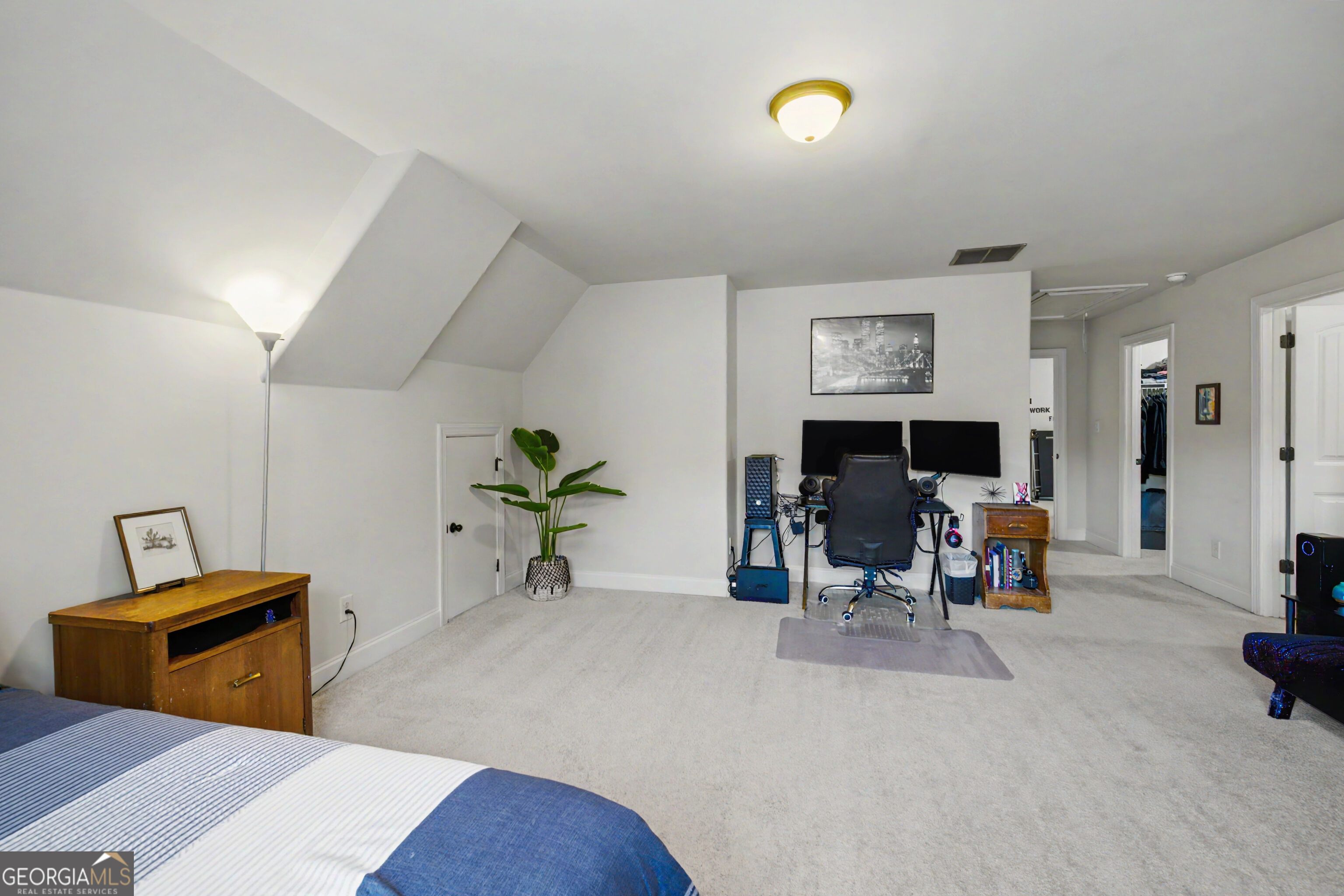 Furnished bedroom with a sloped ceiling and a dual-monitor computer workstation.