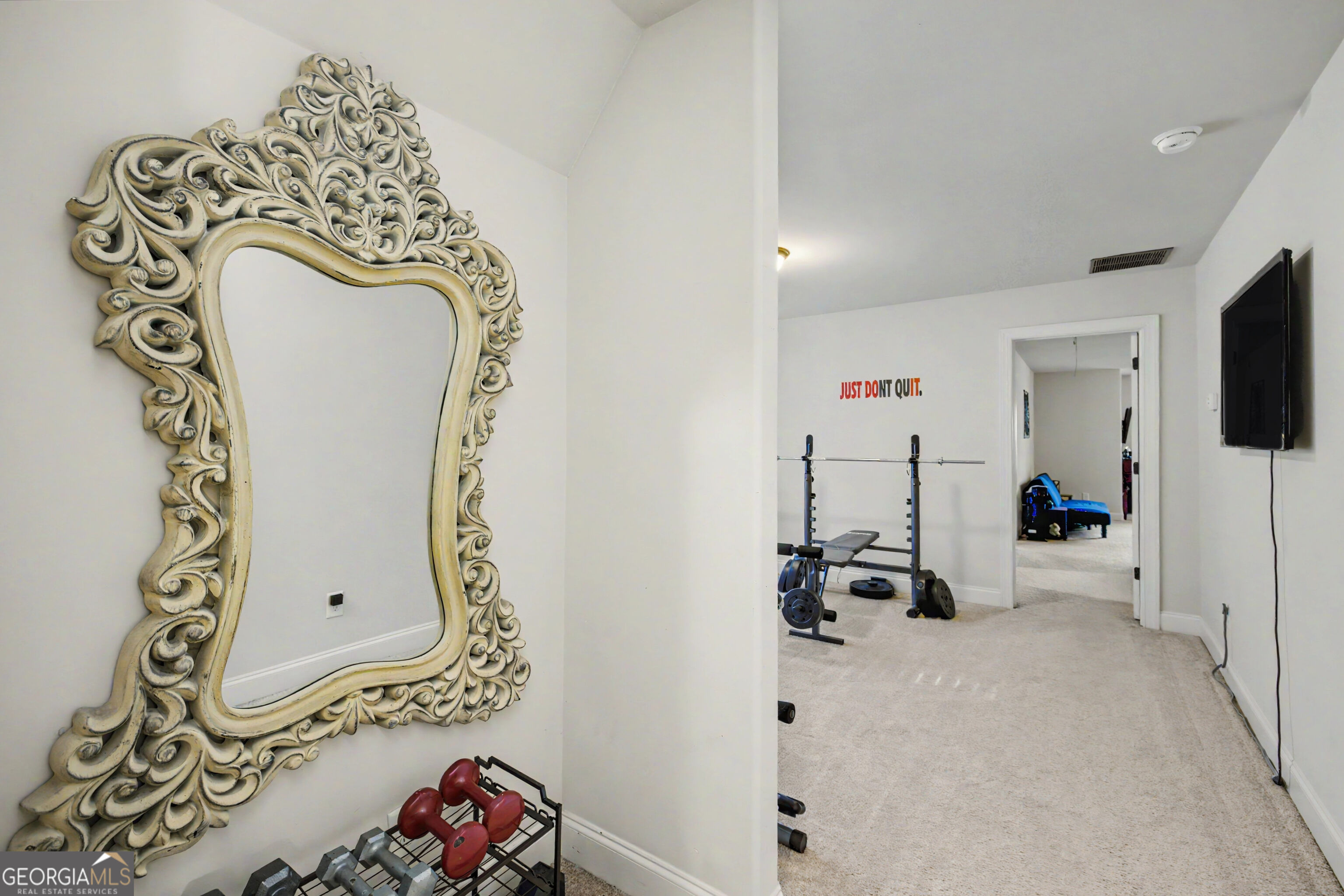 Home gym with weightlifting equipment, an oversized ornate mirror, and a “JUST DON'T QUIT” wall sign.