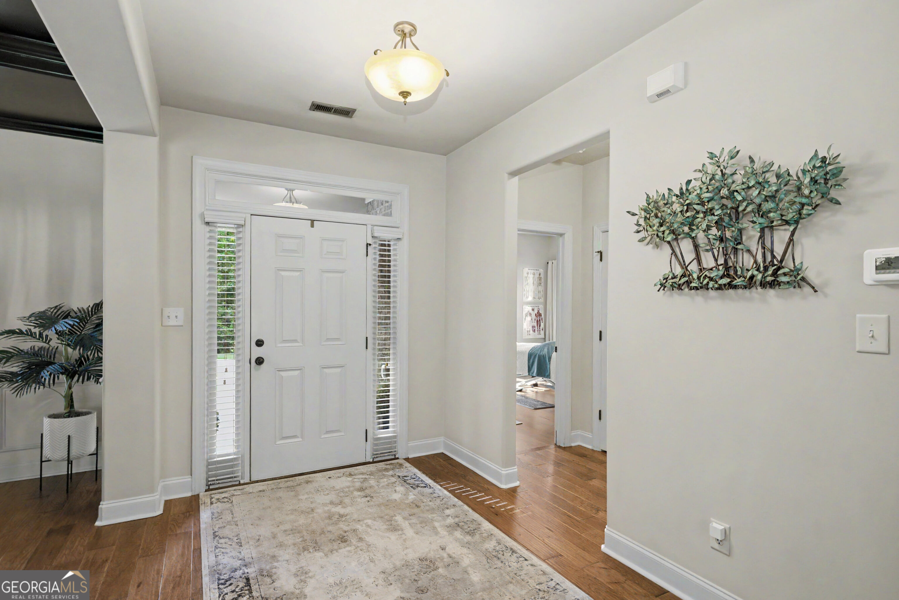 Entry foyer with a white front door, sidelights, hardwood floors, and a large neutral rug.