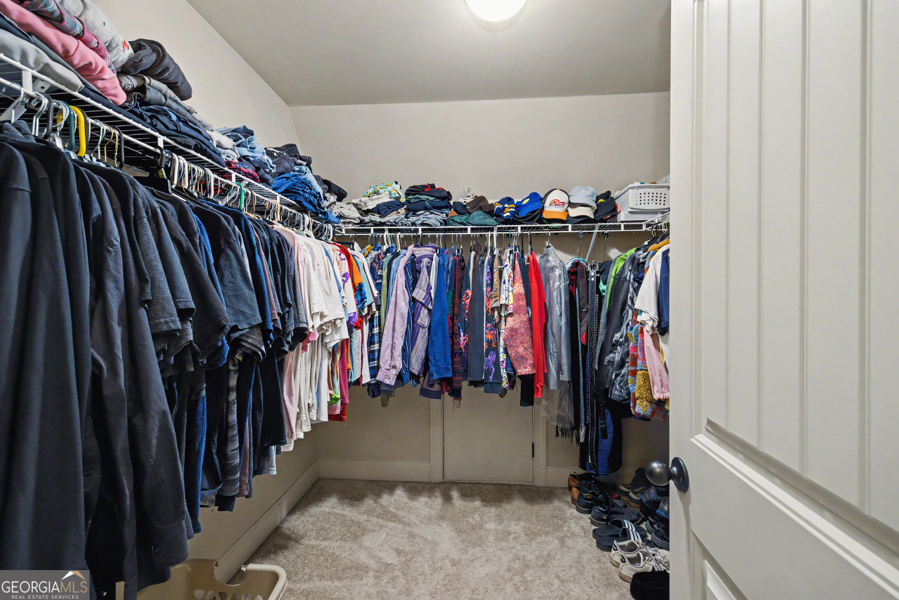 Walk-in closet with clothing on three sides of wire shelving and shoes along the floor.