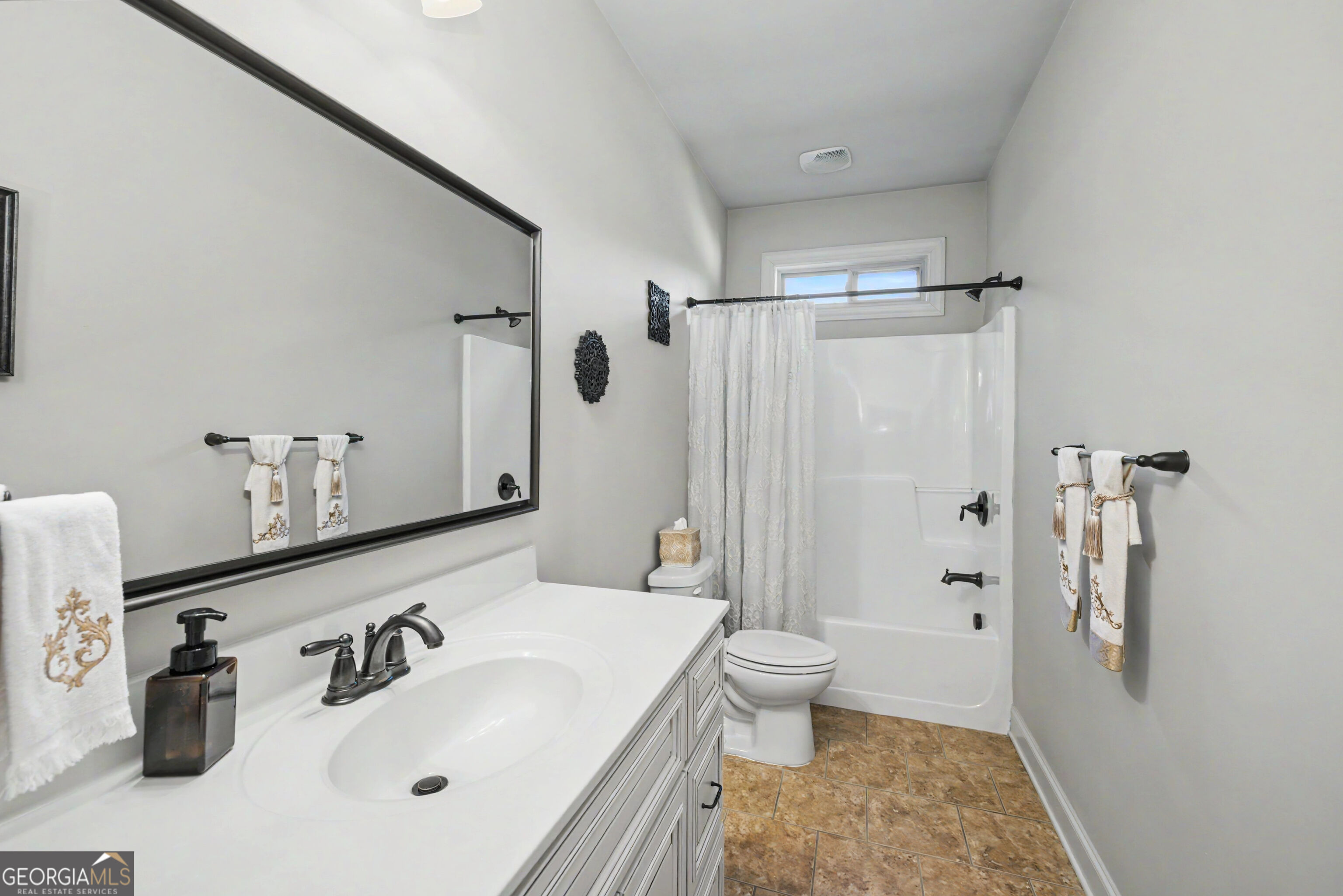Bathroom with a white vanity, large mirror, and tub-shower with a curtain.