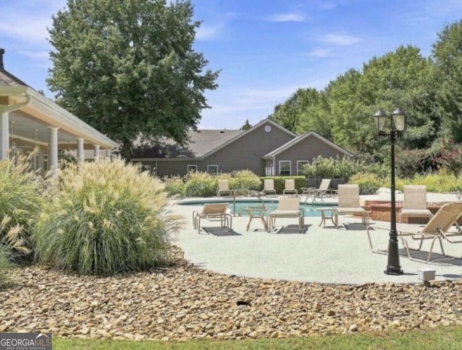 Outdoor swimming pool with lounge chairs, ornamental grasses, and a gray gabled building.