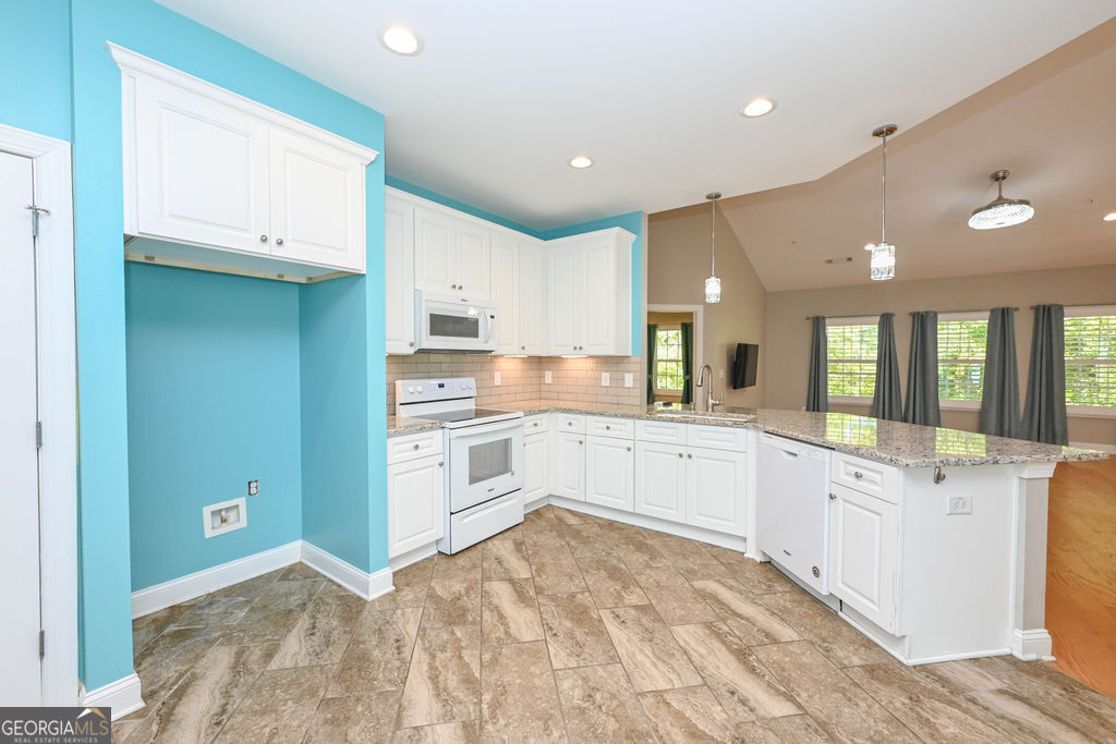 Kitchen with white cabinets, granite island, tan tile floors, and a bold turquoise accent wall.