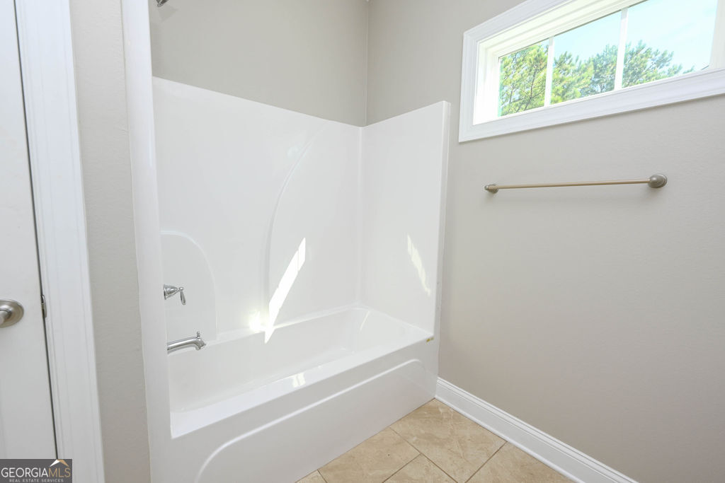 Bathroom with a white tub and shower, beige tile floor, and high window overlooking trees.