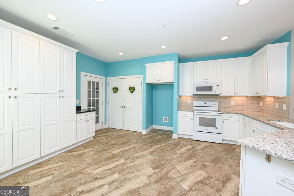 Kitchen with white cabinetry and appliances, turquoise walls, and brown tile flooring.