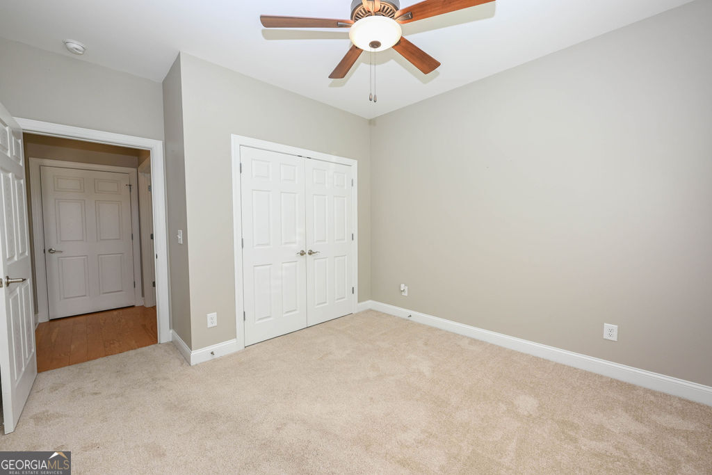 Empty bedroom with beige carpet, a wood-blade ceiling fan, and white double closet doors.