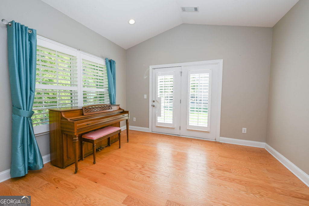 Bright room with a wooden upright piano, teal curtains, shuttered windows, and French doors.