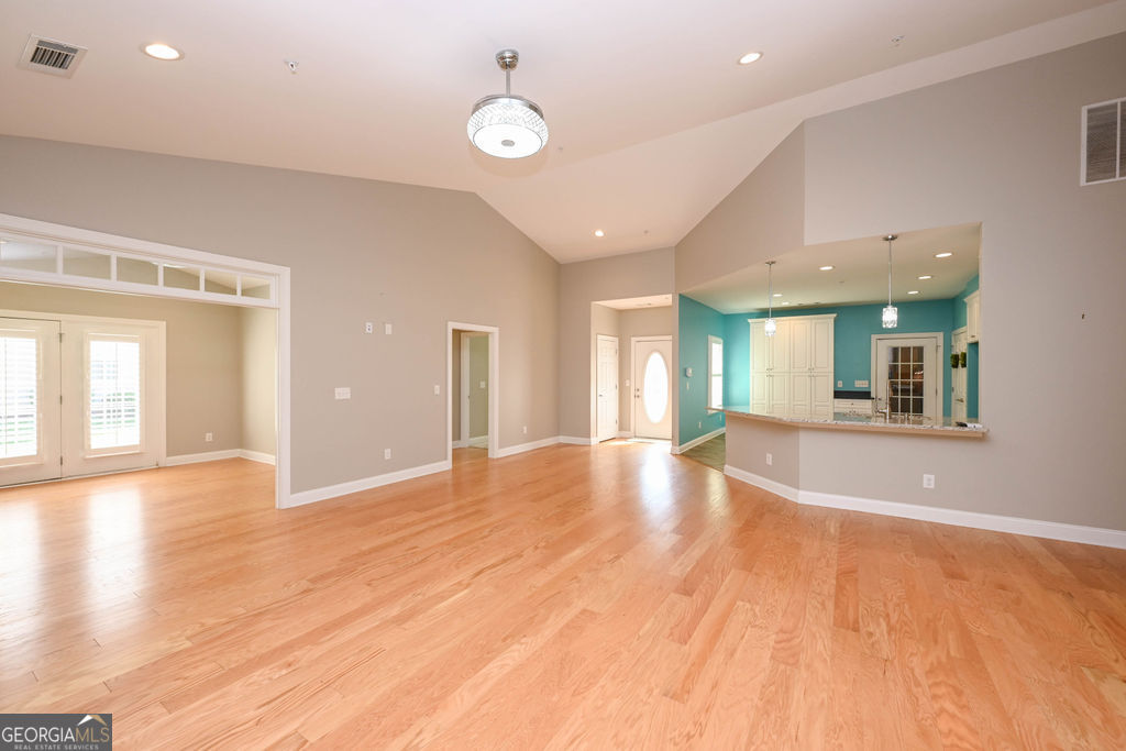 Open living and dining area with hardwood floors, high ceiling, and turquoise kitchen beyond the pass-through.