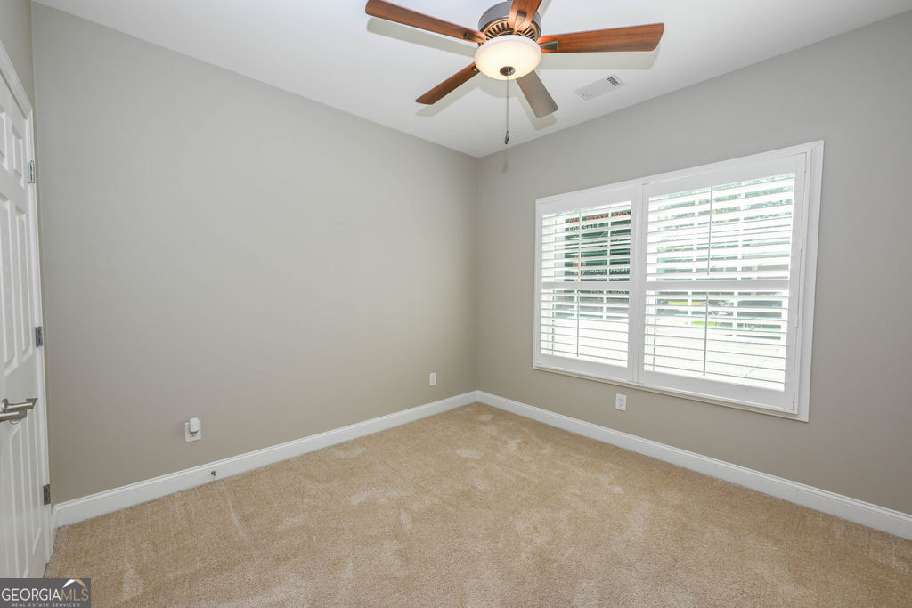 Empty carpeted bedroom with a wood-blade ceiling fan and white plantation shutters.