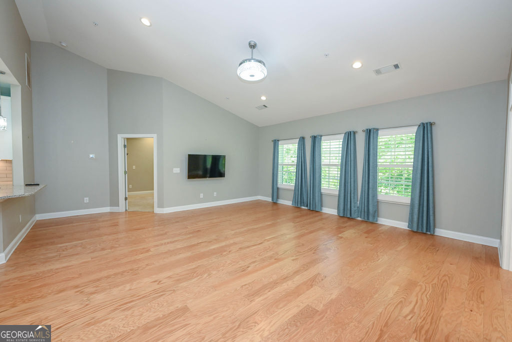 Vacant living room with hardwood floors, a vaulted ceiling, and three curtained windows.