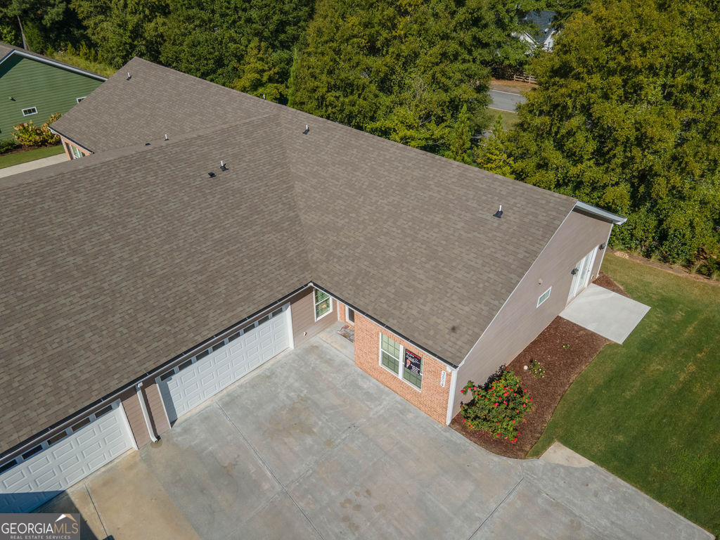 Aerial view of a home with a broad gray roof, attached garages, and a concrete driveway.