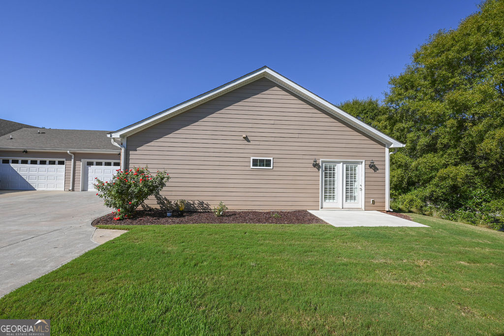 Home exterior with white-trimmed patio doors, attached garage, and green lawn.