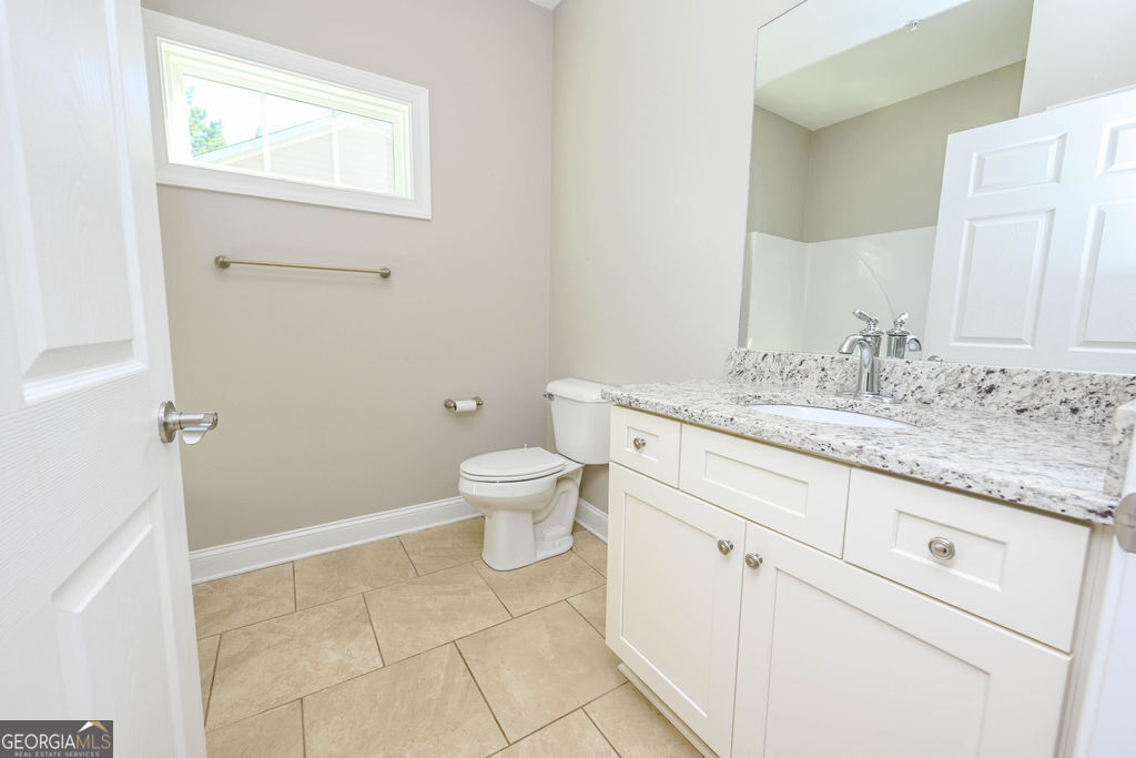 Bathroom with a white vanity, speckled stone countertop, and high window.