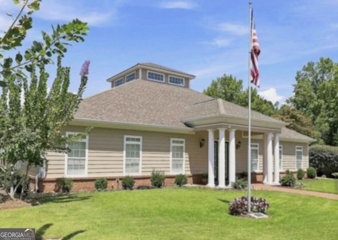 Tan-sided building with a brick base, raised cupola, and columned entrance beside a flagpole and lawn.