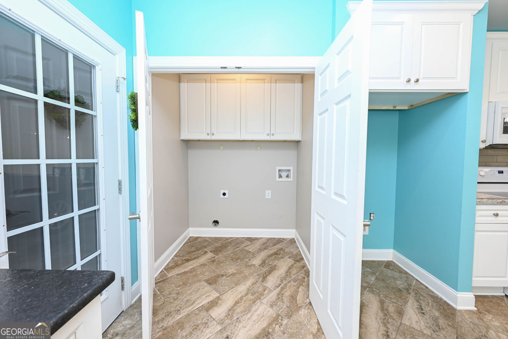 Laundry alcove with white cabinets, washer hookups, and patterned tile flooring.