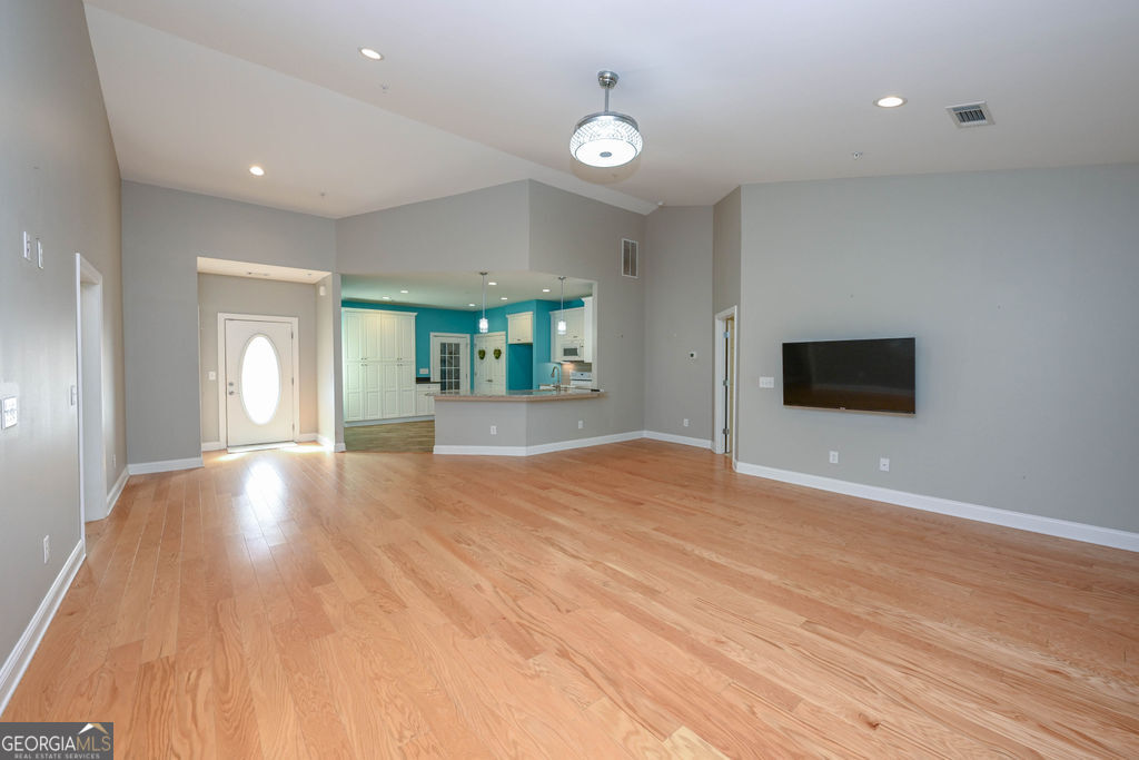 Unfurnished living room with hardwood floors, a wall-mounted TV, and an open turquoise-and-white kitchen.