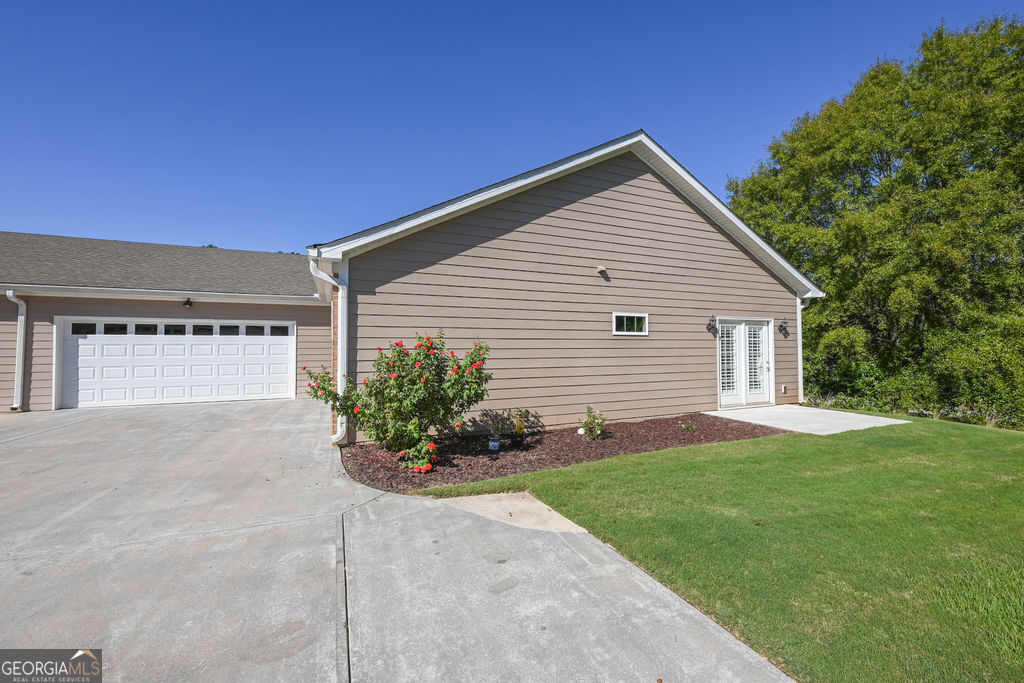 Gray-sided home with a two-car garage, wide concrete driveway, and flowering shrubs.