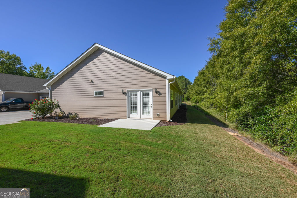 Tan-sided home with white double doors opening onto a small concrete patio.