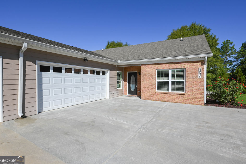 Single-story home with brick and taupe siding, a white double garage door, and a broad concrete driveway.