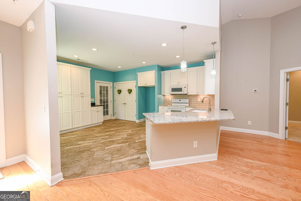 Open kitchen with white cabinets, teal walls, and a granite-topped peninsula with sink.