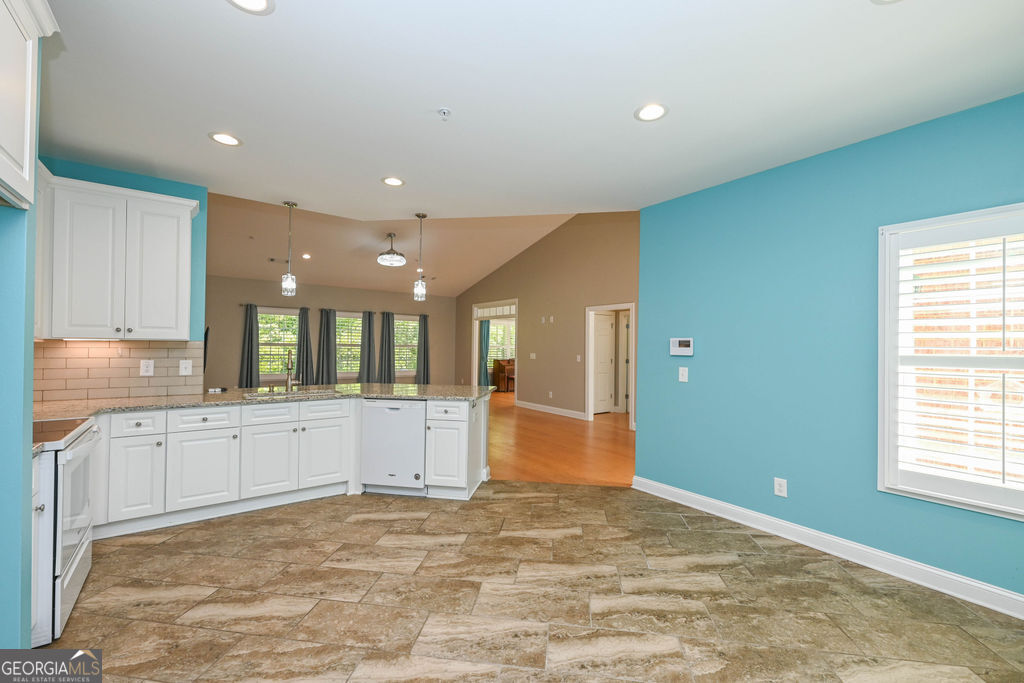 Kitchen with white cabinetry, a peninsula, tan tile flooring, and turquoise walls opening to a living area.