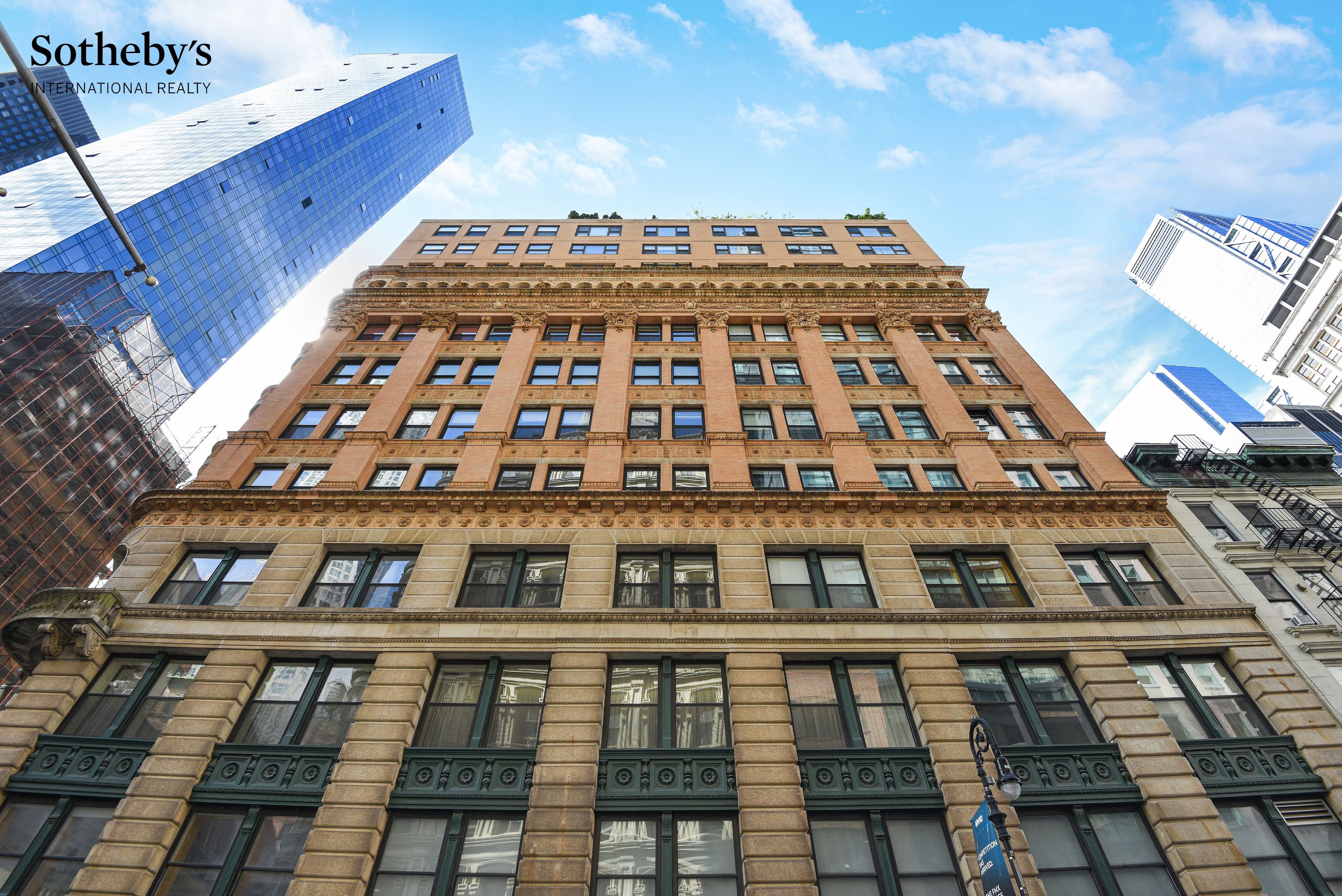 Ornate tan-brick apartment building viewed from below, with carved stone details and city towers around it.