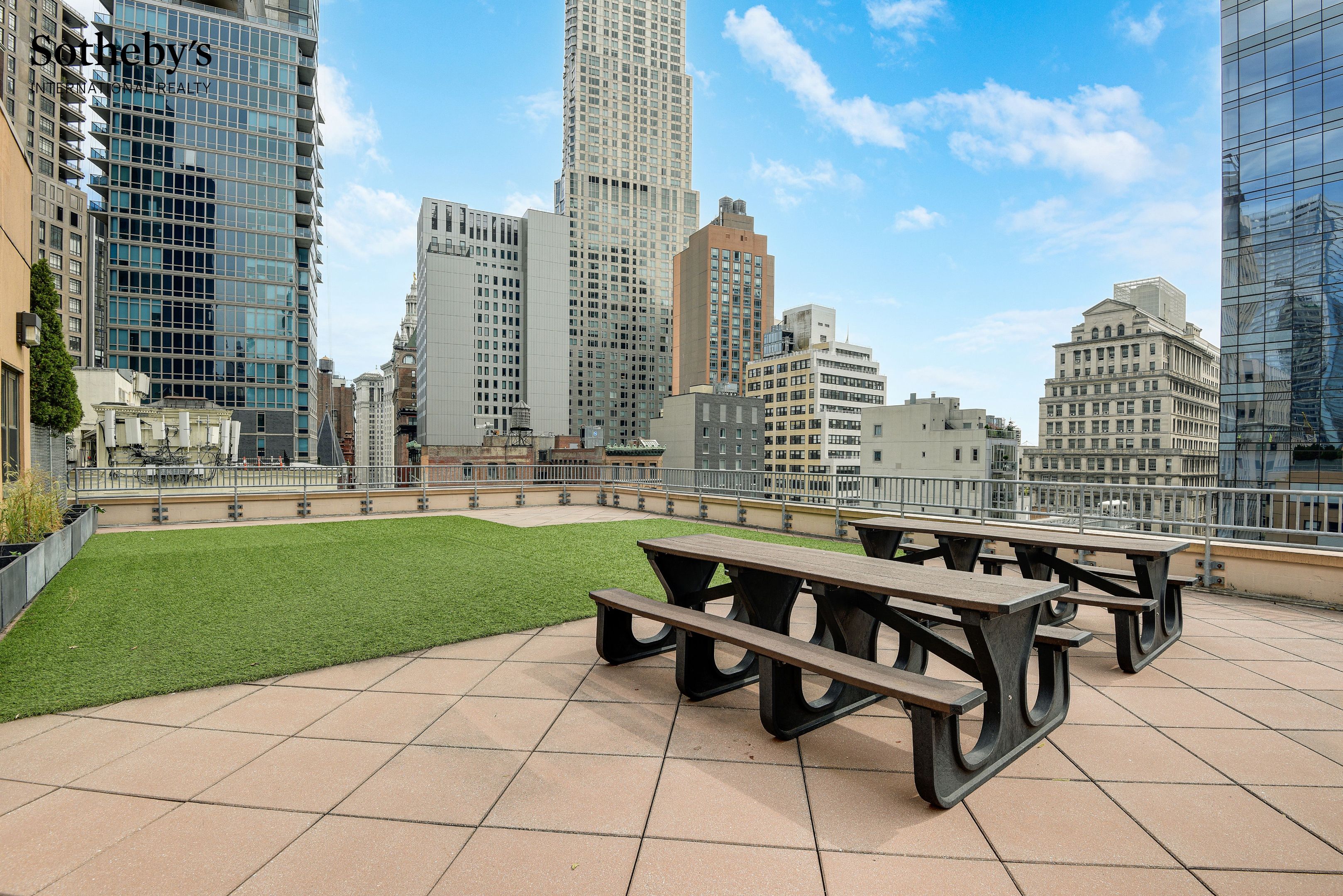 Rooftop terrace with picnic tables, a lawn, and surrounding Manhattan skyscrapers.