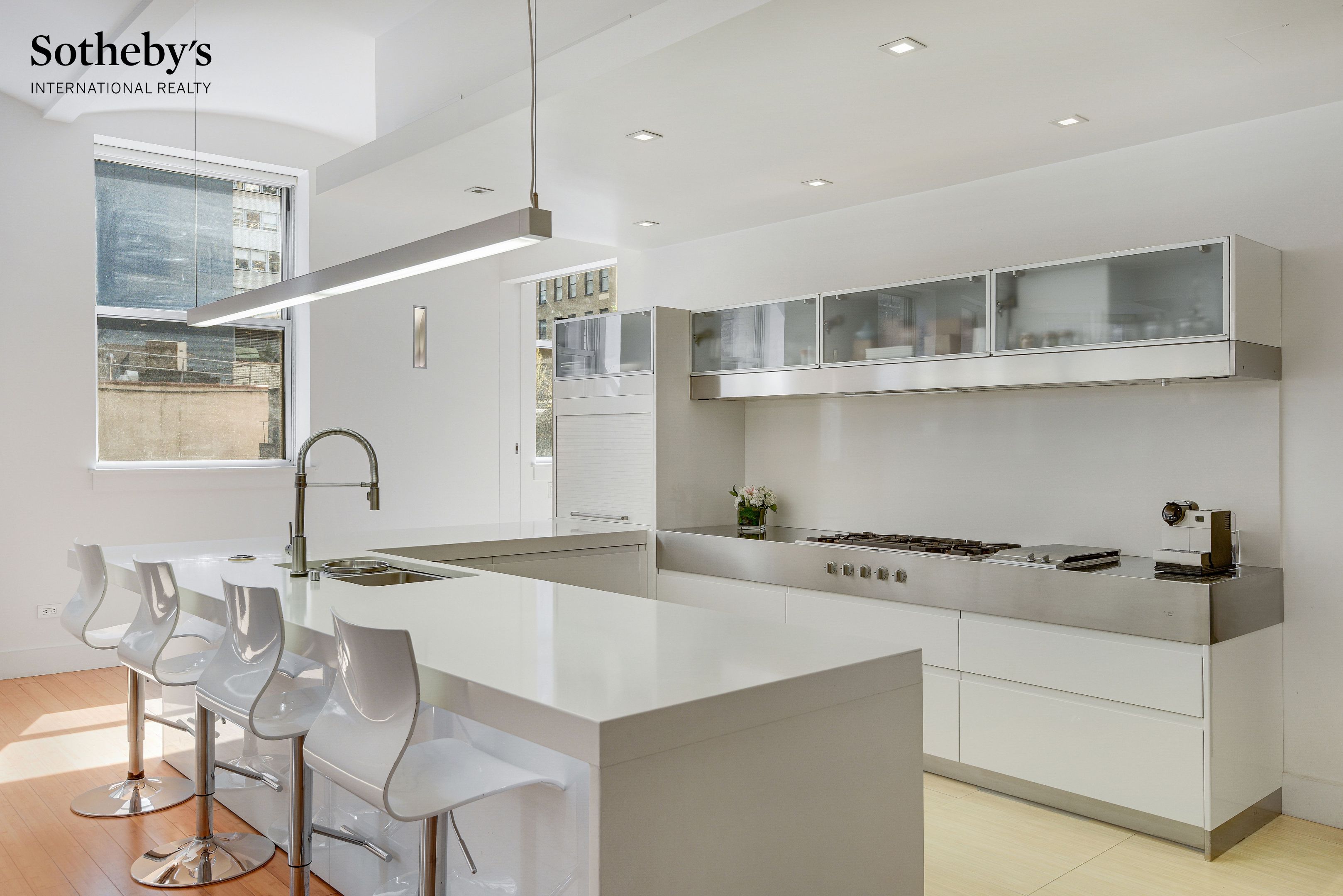 Modern white kitchen with a large island, bar stools, and stainless-steel appliances.
