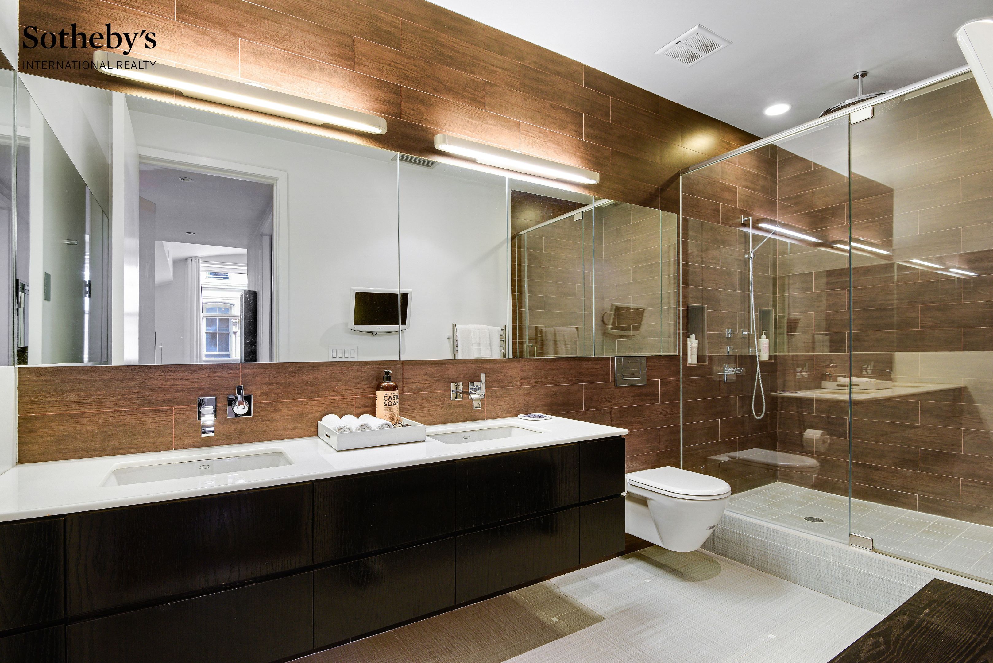 Modern bathroom with a double-sink vanity, wood-look tile, and glass-enclosed shower.