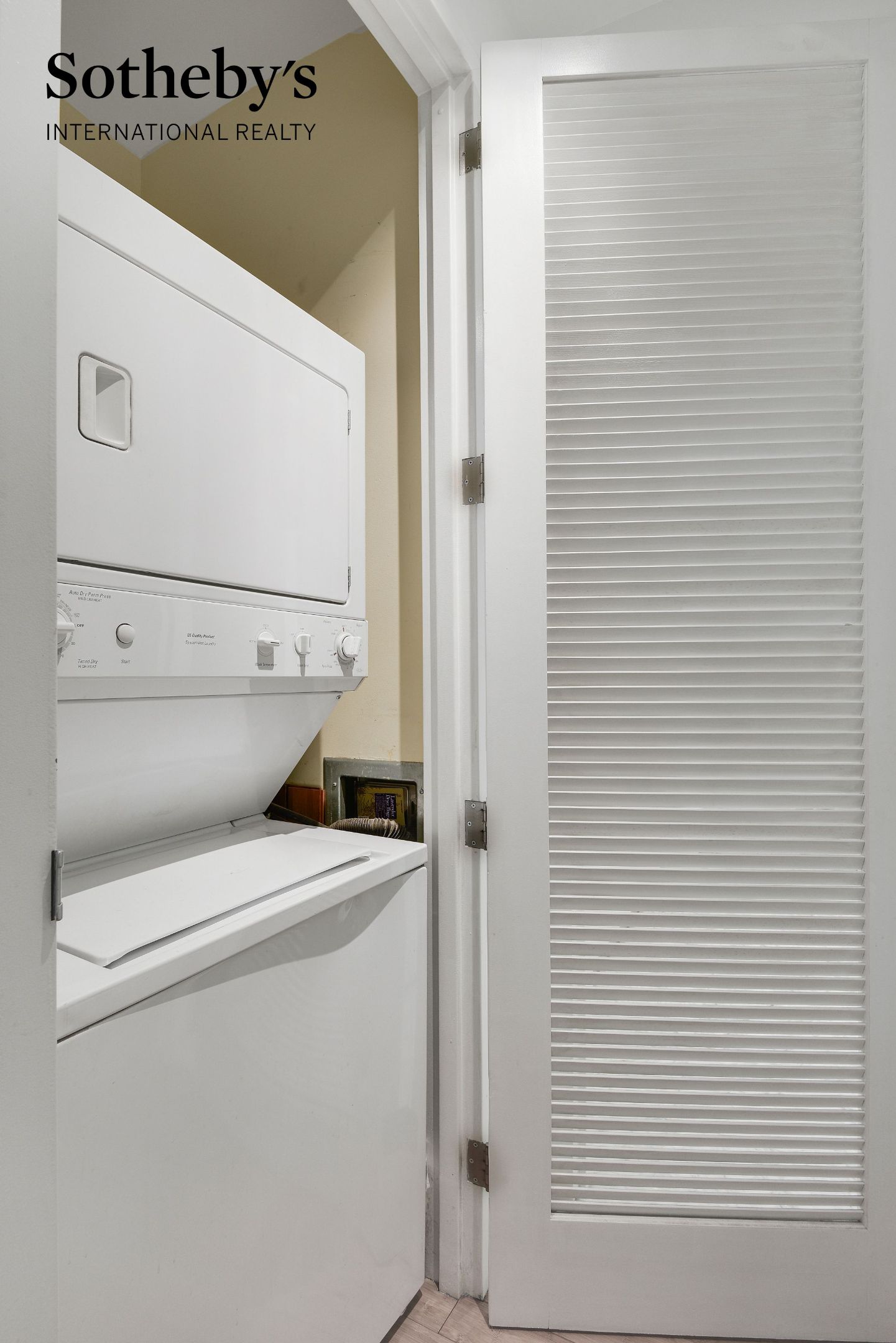 Laundry closet with a stacked washer and dryer behind a louvered door.