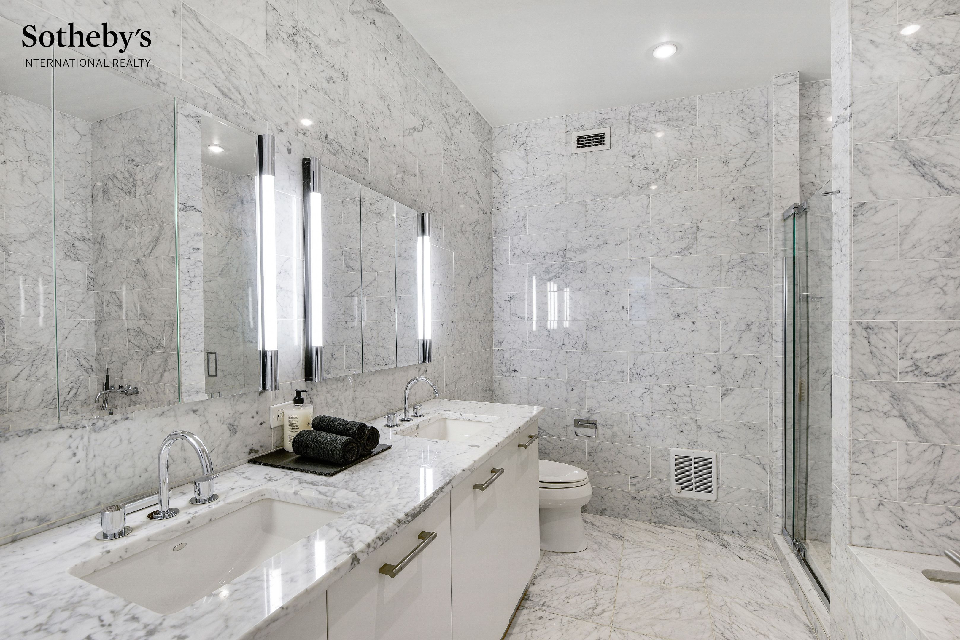 Marble bathroom with double vanity, illuminated mirrors, and glass-enclosed shower.