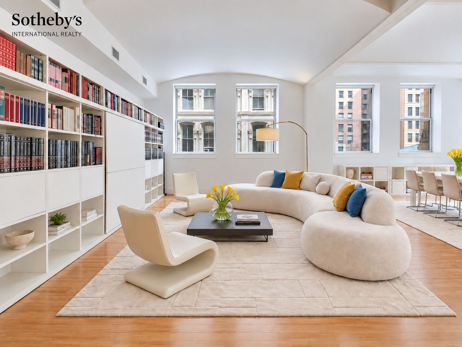 Bright living room with floor-to-ceiling bookshelves, a curved sofa, and large windows.
