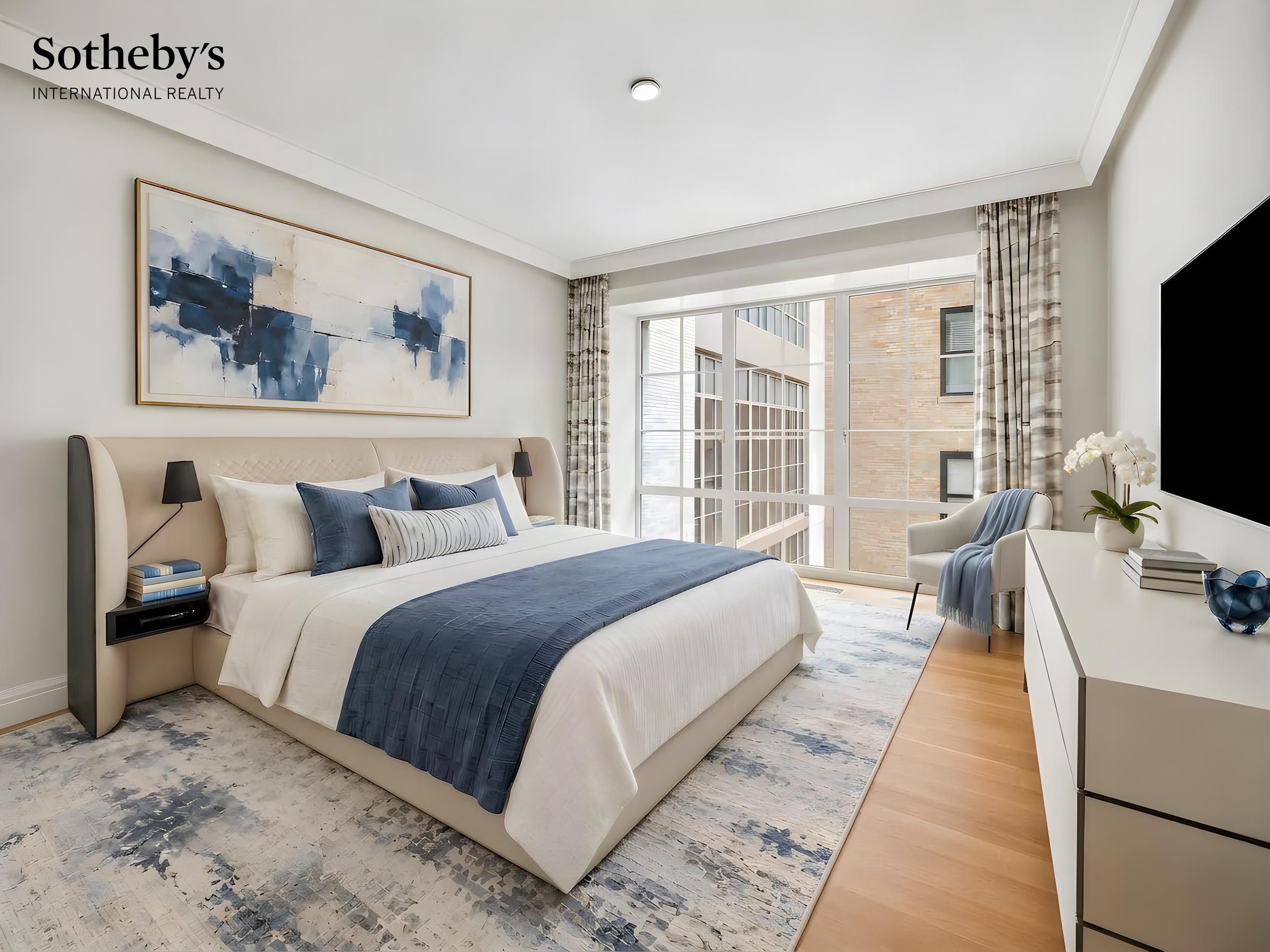 Furnished bedroom with a white-and-navy bed, abstract wall art, and large windows overlooking a nearby building.