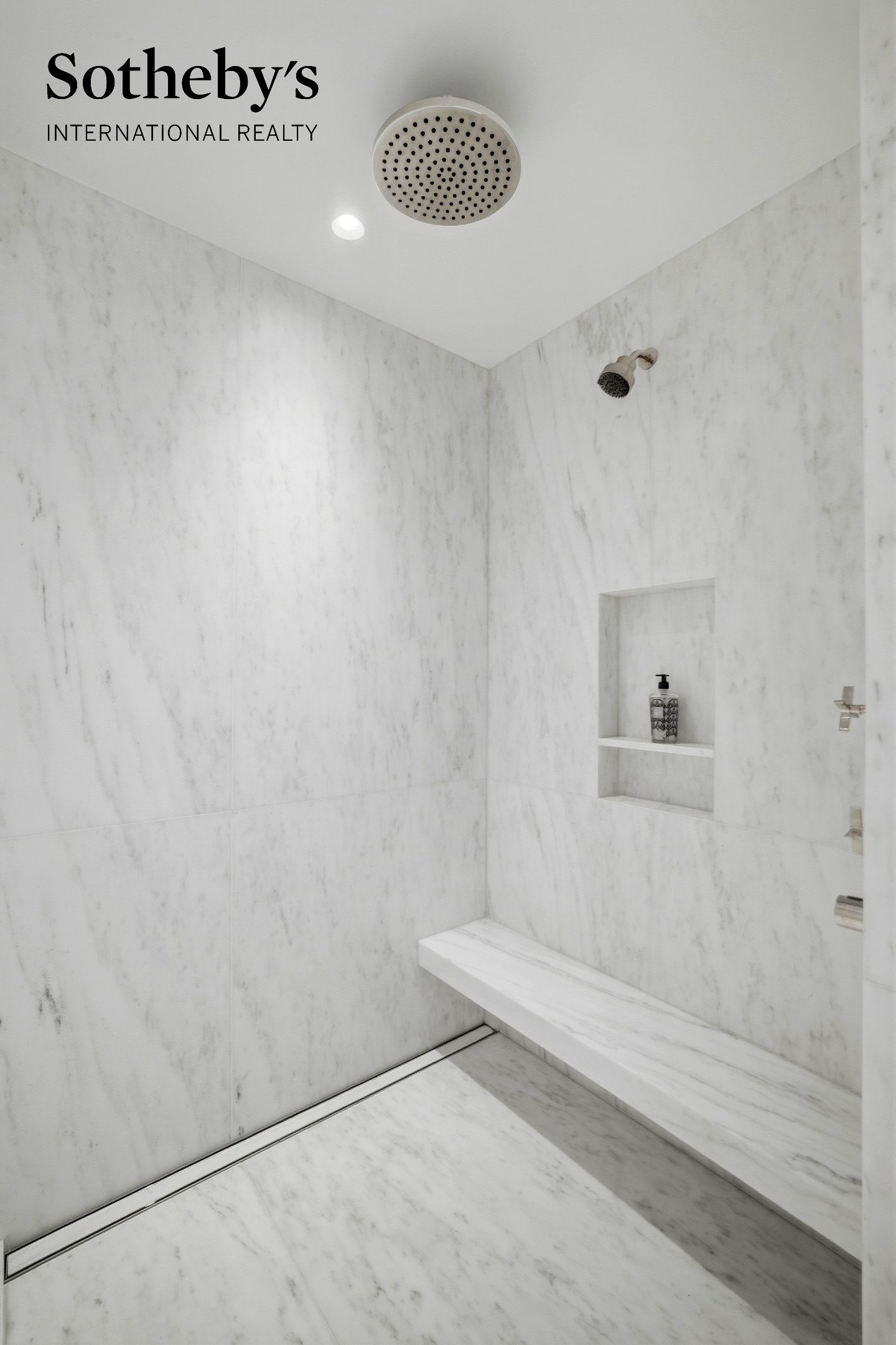 Marble shower with a ceiling-mounted rainfall head, built-in bench, recessed niche, and linear drain.