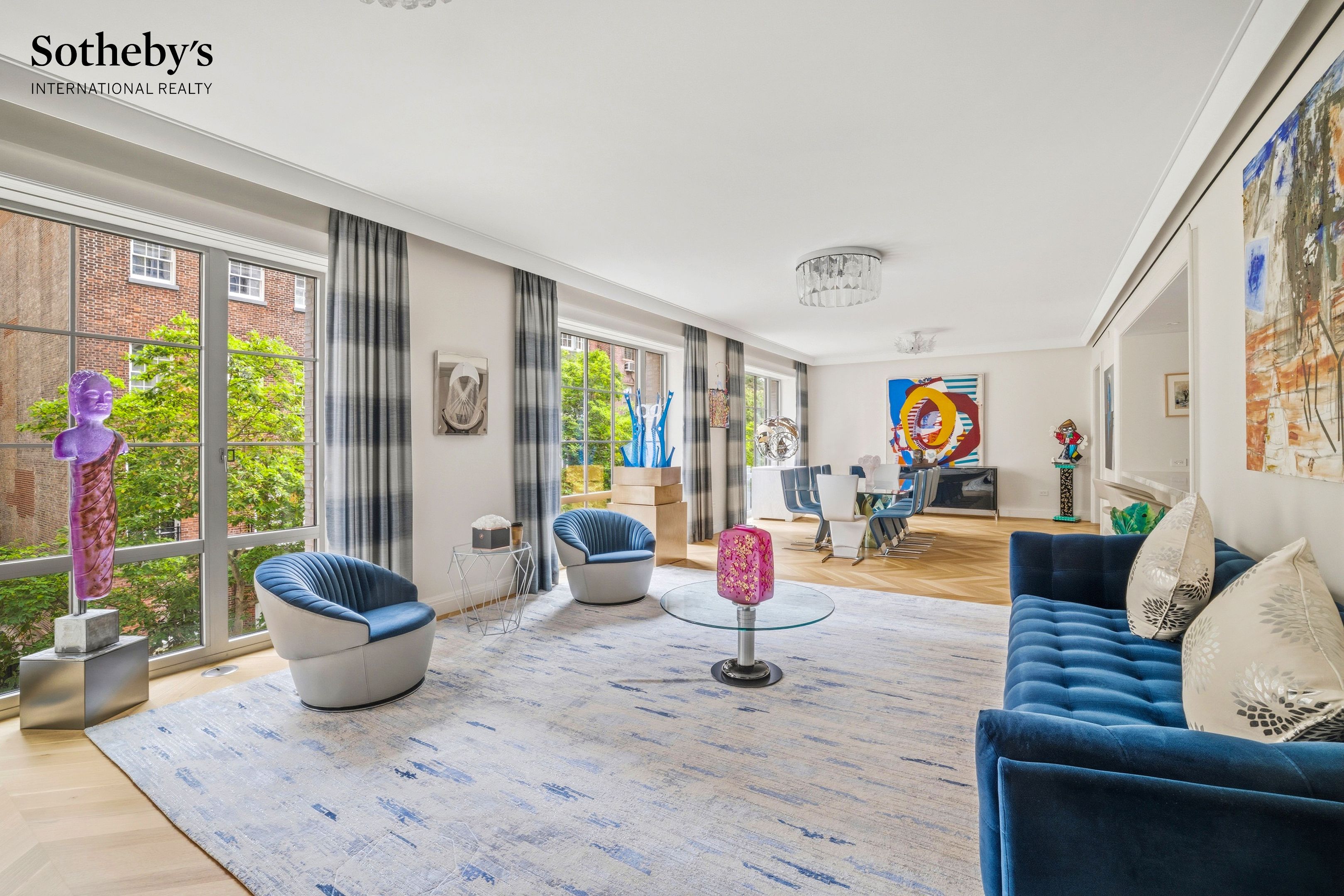 Bright living and dining room with blue seating, floor-to-ceiling windows, and colorful contemporary art.