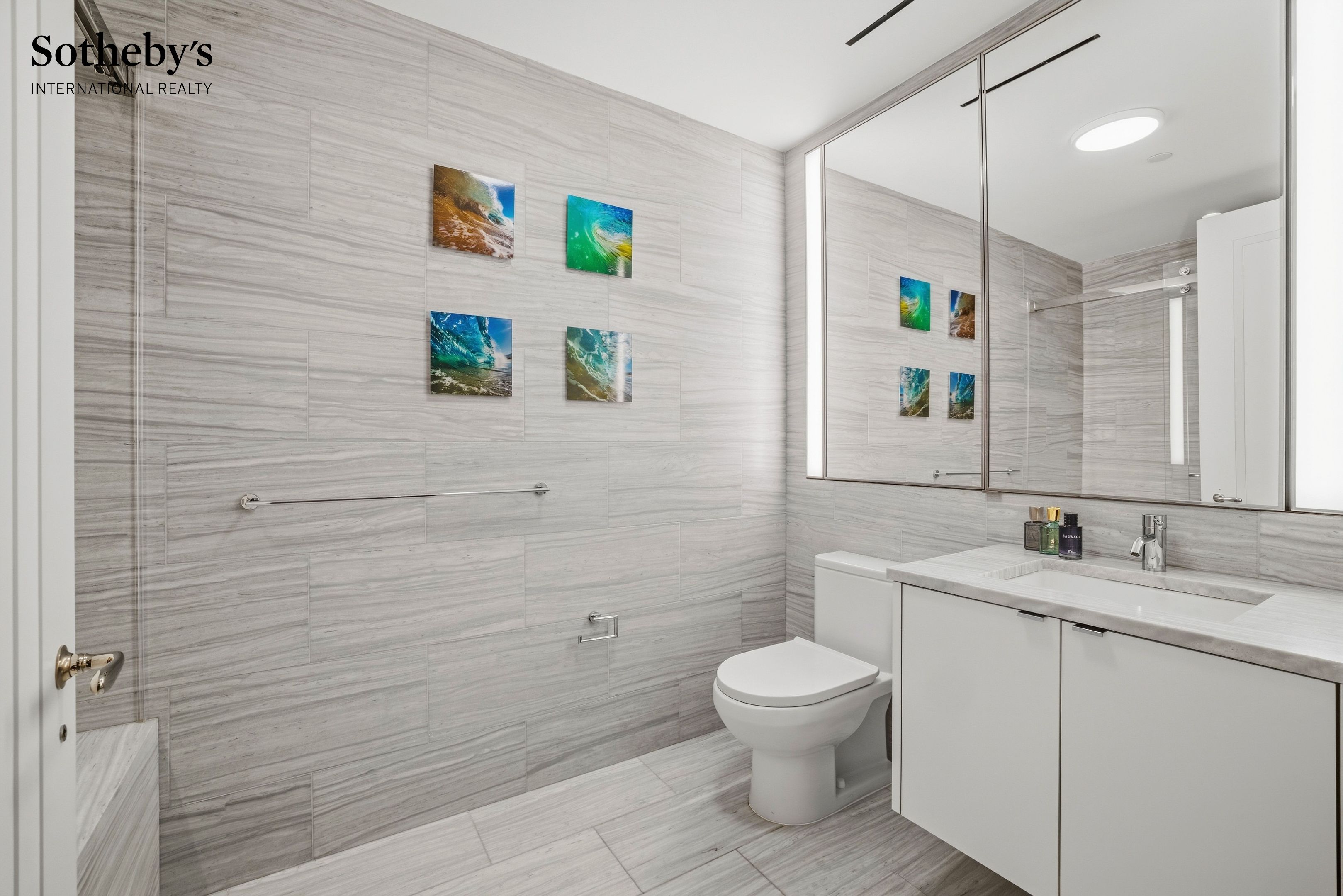 Modern gray-tiled bathroom with a white vanity, mirrored cabinet, and colorful wave prints.