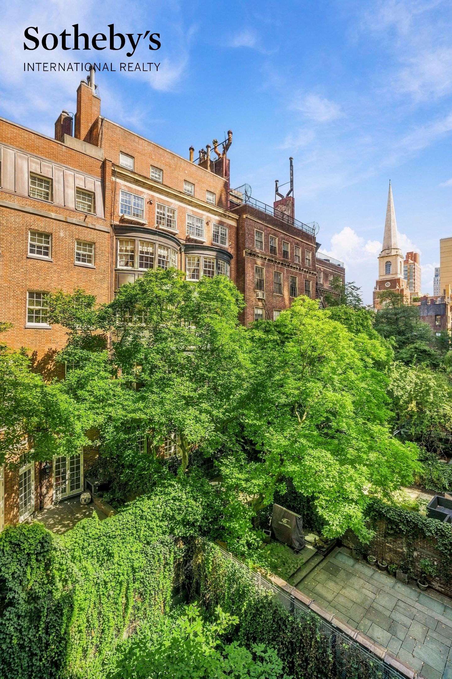 Leafy courtyard garden between brick apartment buildings, with a church spire beyond.