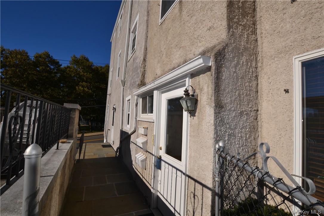 Stucco home’s side entrance with a white door, wall lantern, and narrow walkway.